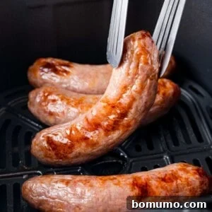 Air fryer brat being lifted out of the air fryer with tongs.