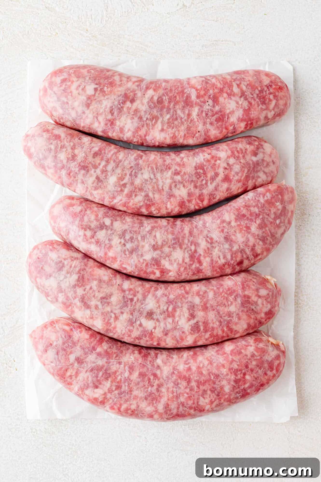 Five uncooked brats on a white surface.