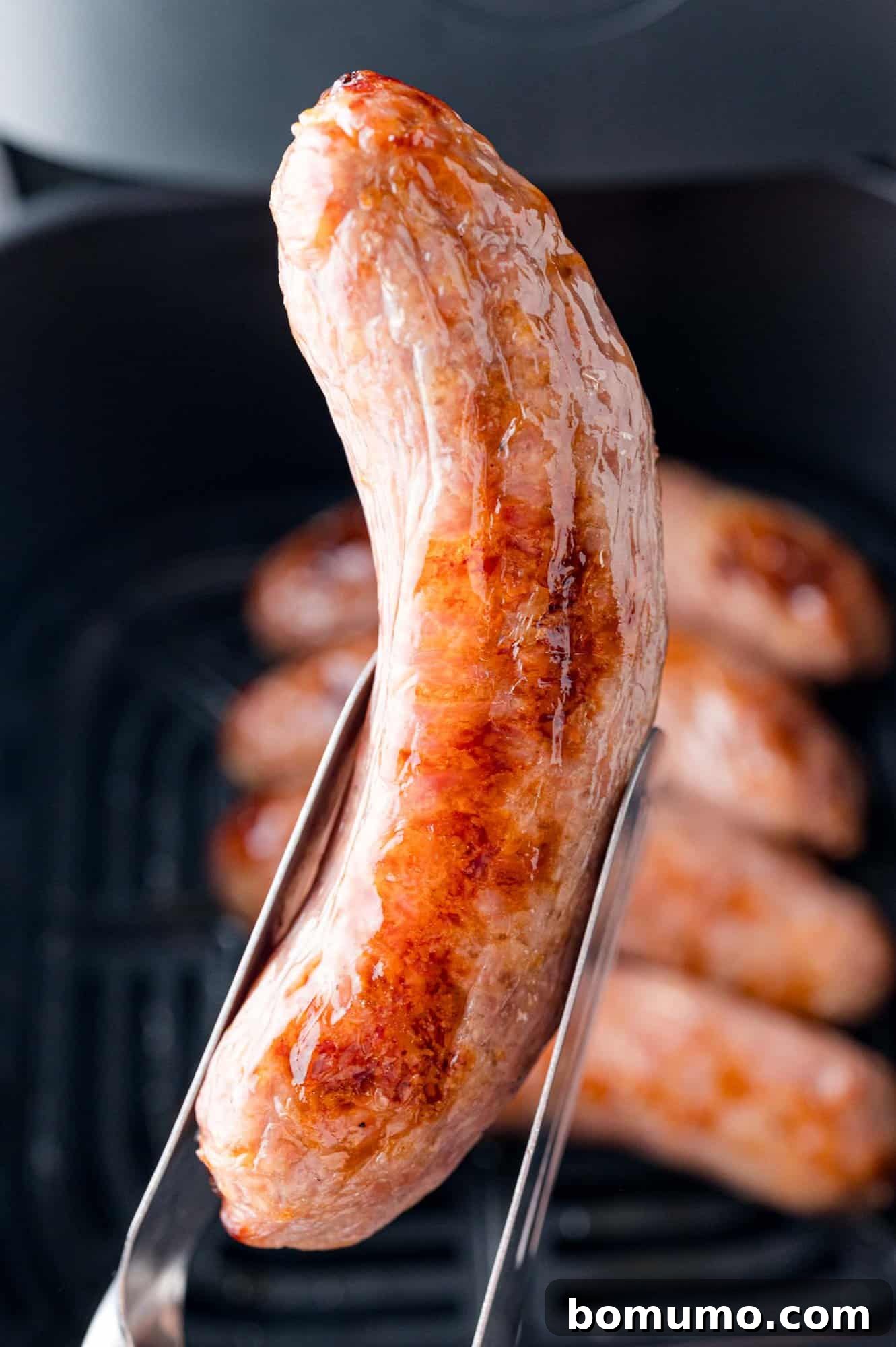 Air fryer brat being held with tongs.