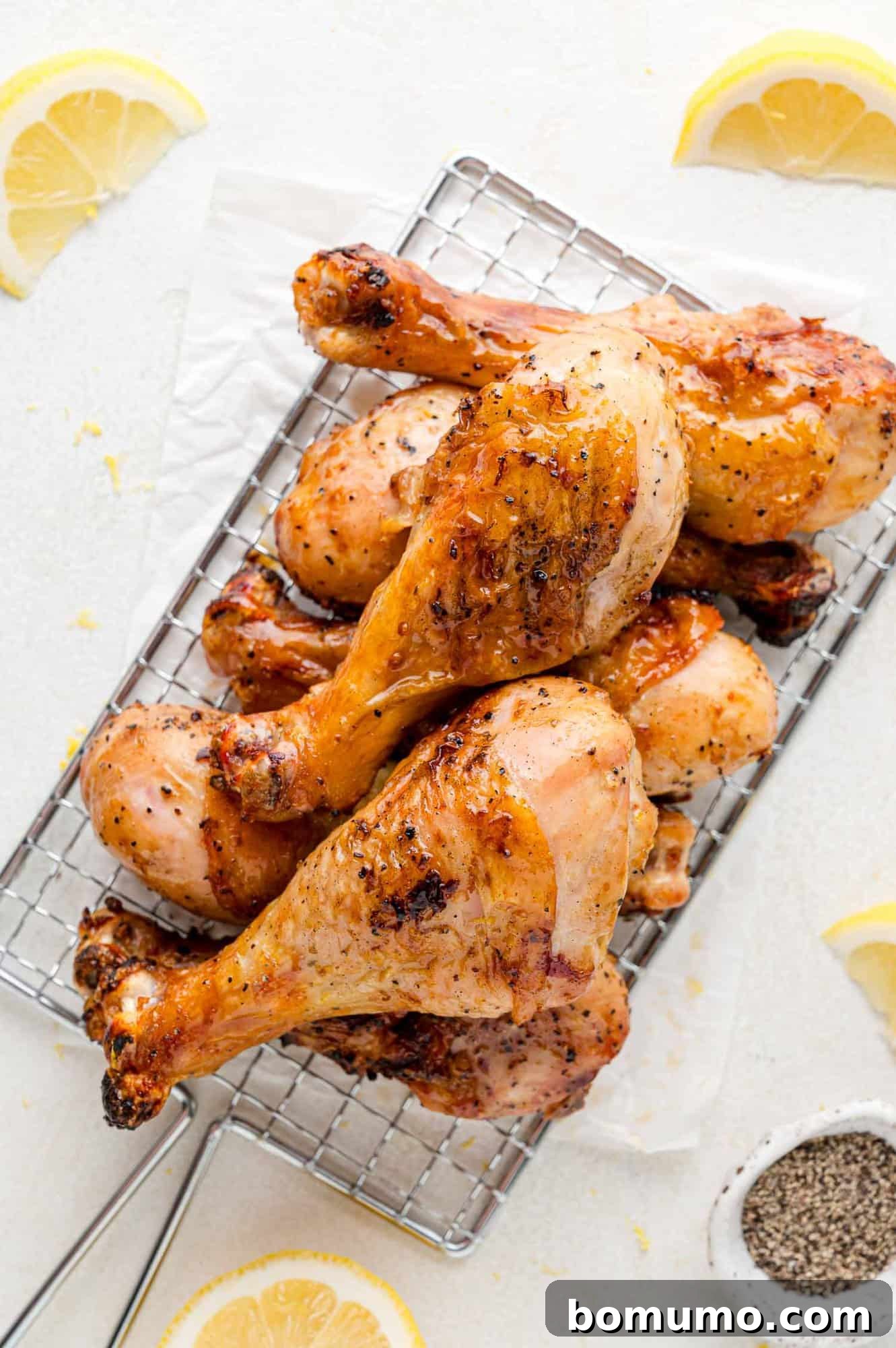 Stack of perfectly grilled chicken drumsticks piled high, adorned with fresh lemon wedges, highlighting the vibrant flavors of the lemon pepper marinade.