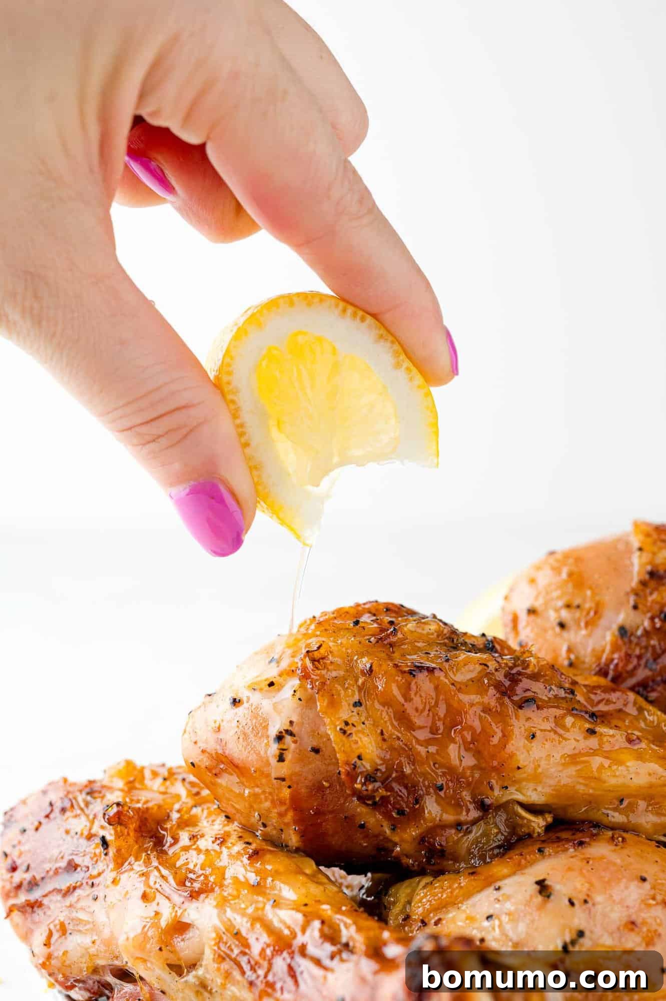 A vibrant lemon being freshly squeezed over a plate of hot, grilled chicken drumsticks, enhancing the zesty aroma and flavor.