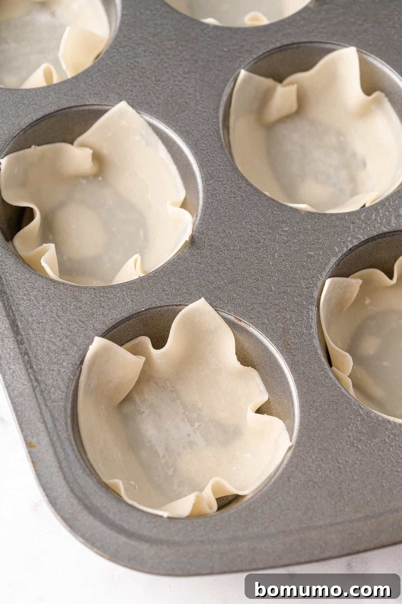 Wonton wrappers pressed into a muffin tin.