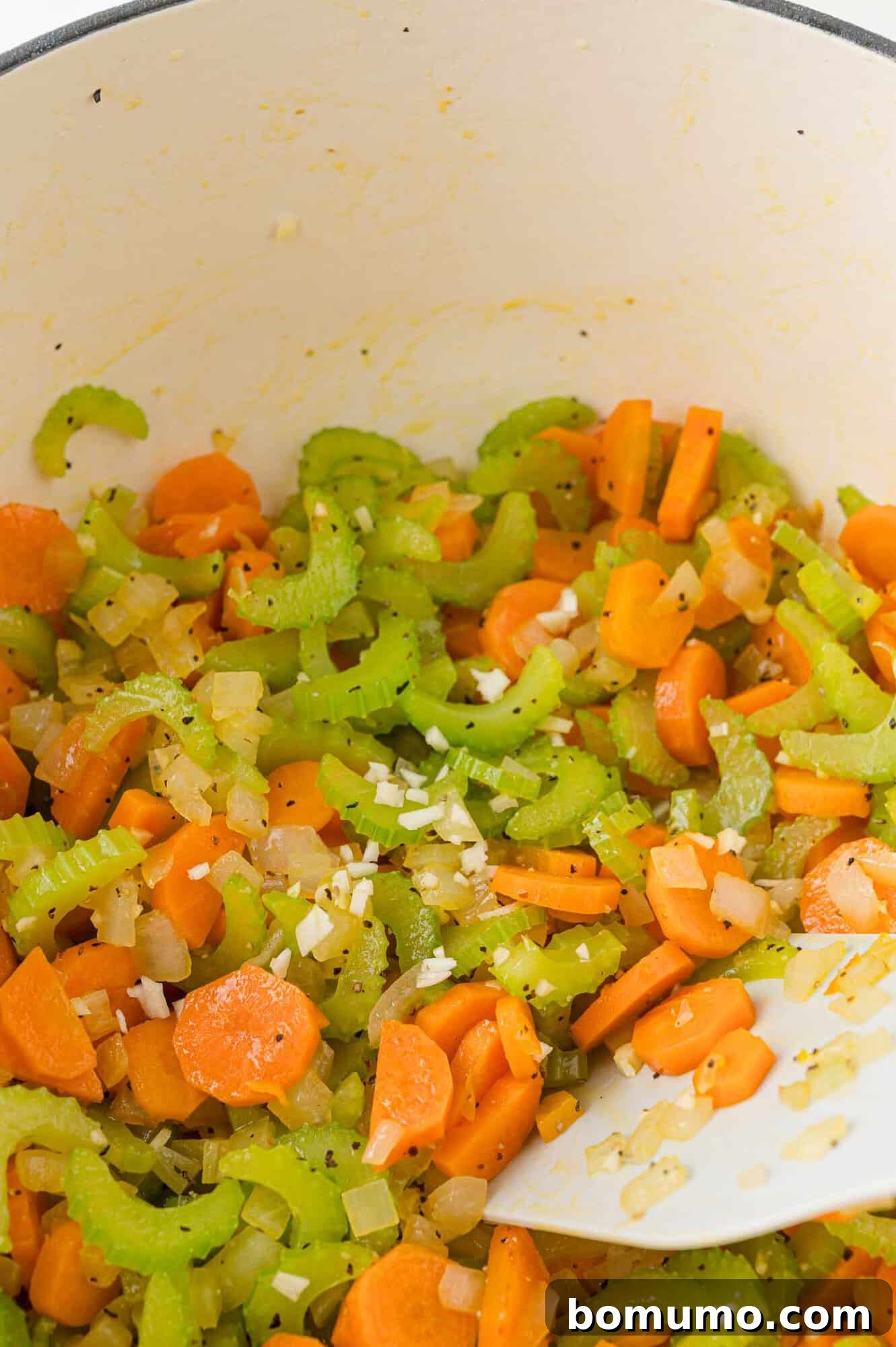 Vegetables being sautéed in a large pot.