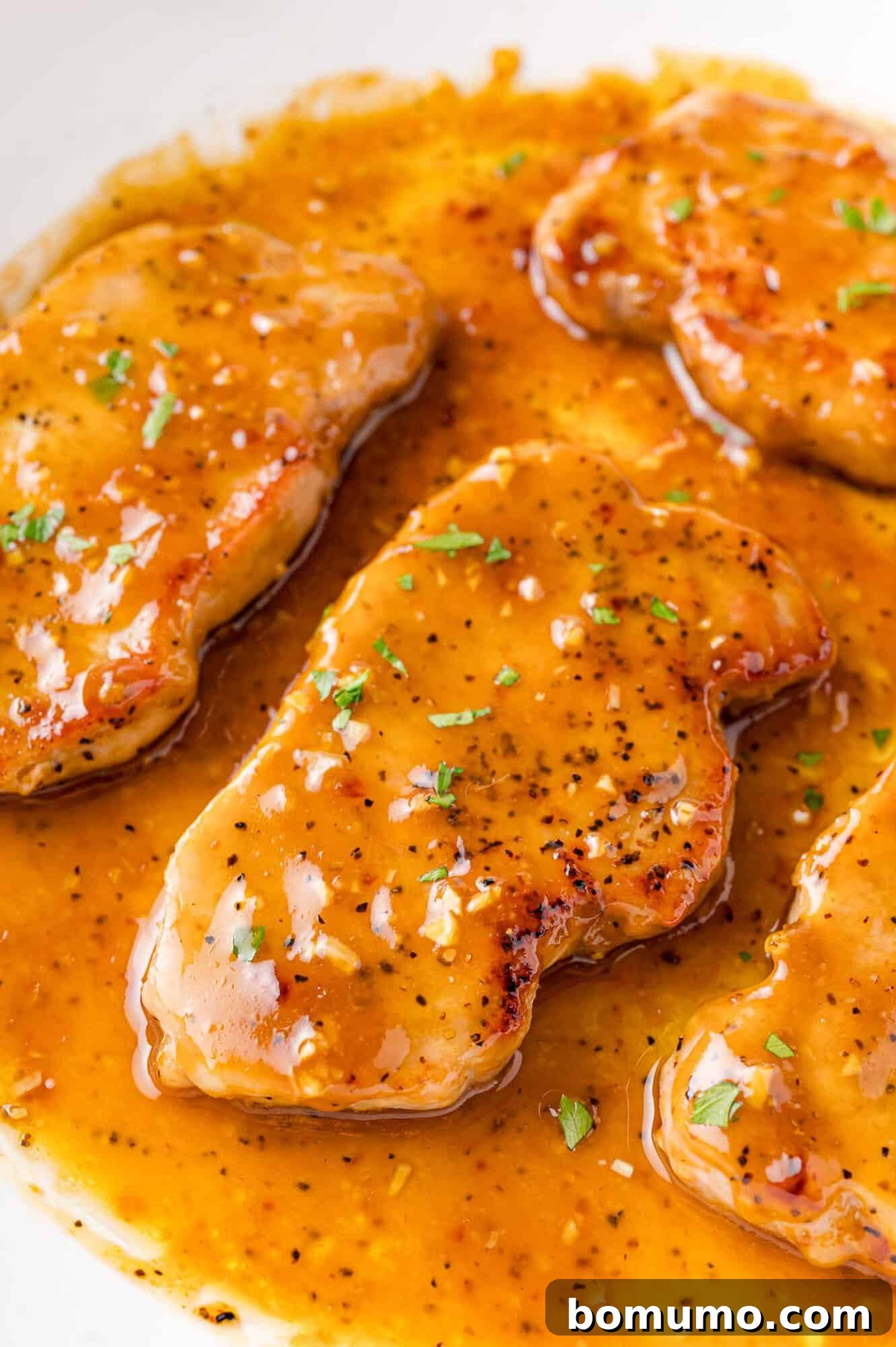 Honey garlic pork chops still in pan, glistening with sauce.