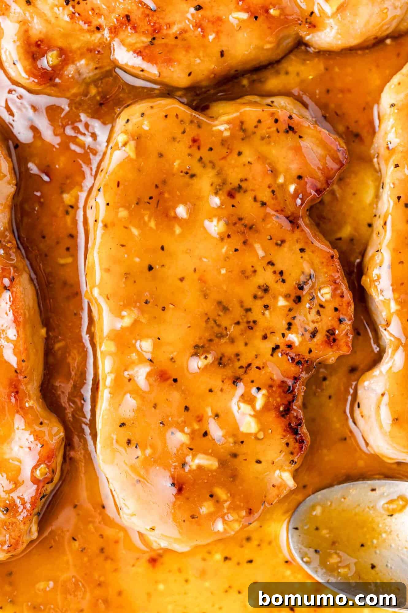Honey garlic pork chop in pan, being coated with the sauce.