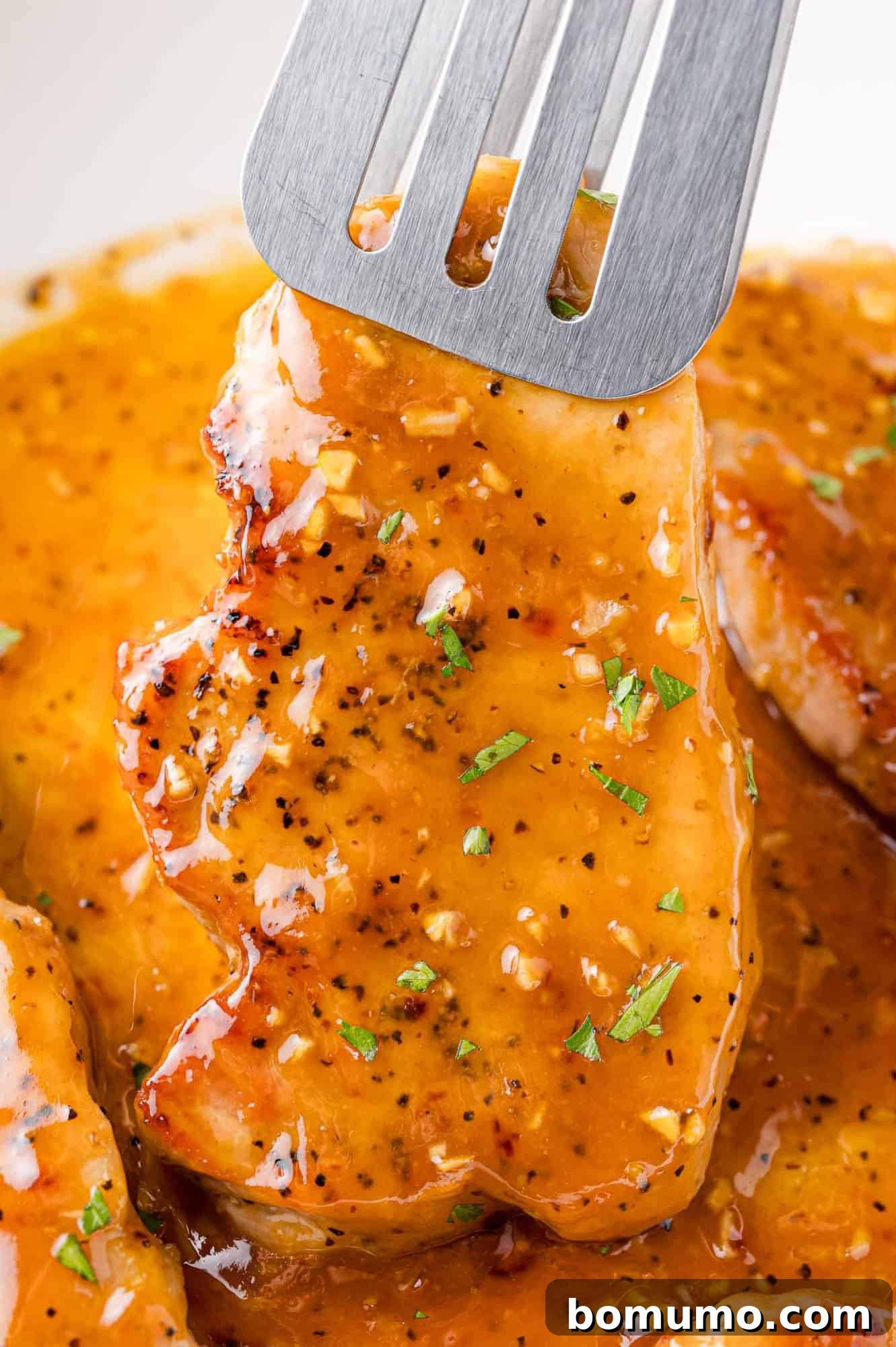 Pork chop being lifted up with tongs, showcasing the glossy sauce.