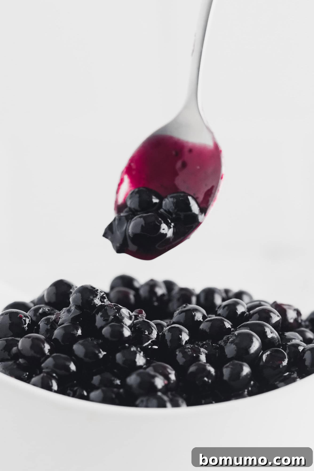 Luscious Blueberry Compote 7 Homemade blueberry sauce being gracefully scooped from a pristine white bowl with a spoon, highlighting its rich texture and appealing color.