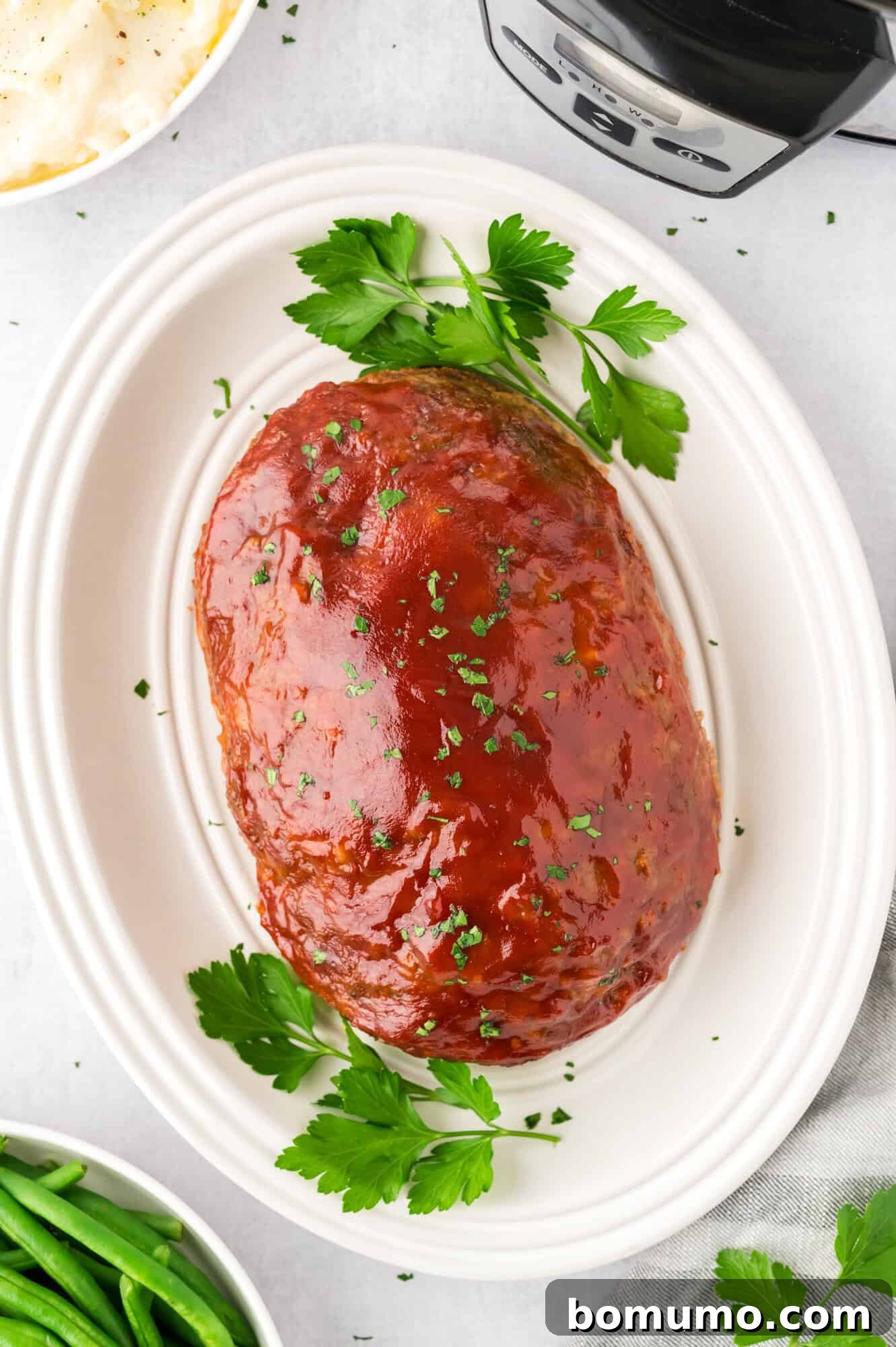 The finished crockpot meatloaf placed on a white platter and garnished with fresh parsley sprigs.