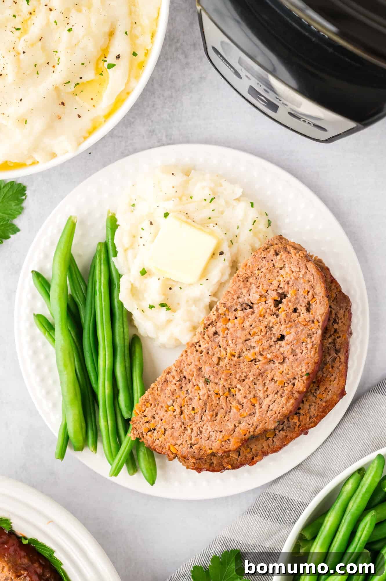 A serving of glazed meatloaf on a plate, accompanied by creamy mashed potatoes and vibrant green beans.