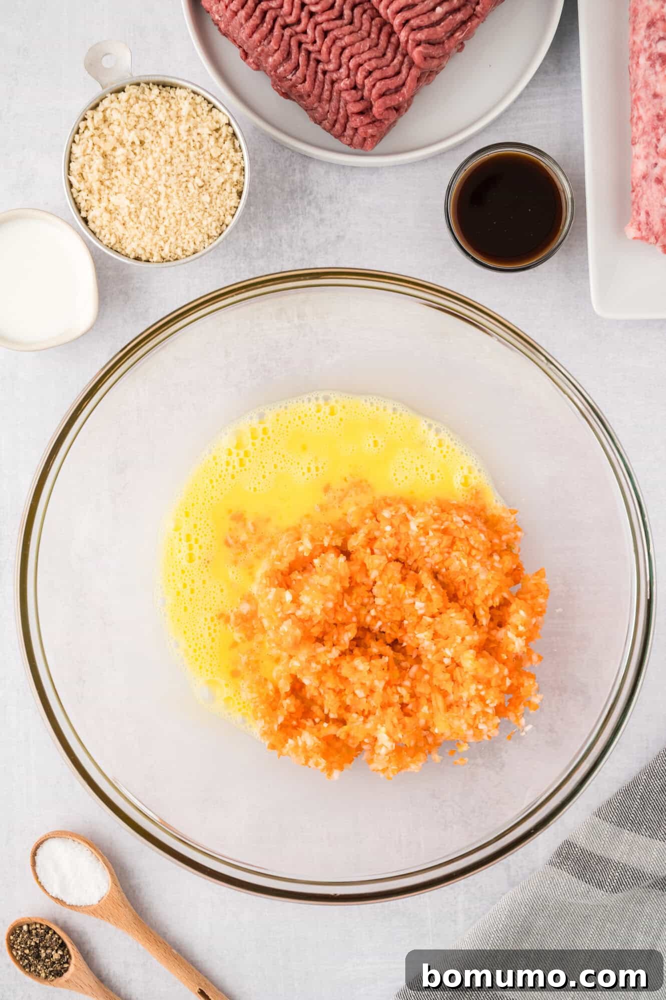 Whisked eggs and minced vegetables in a clear glass mixing bowl, ready for meatloaf preparation.