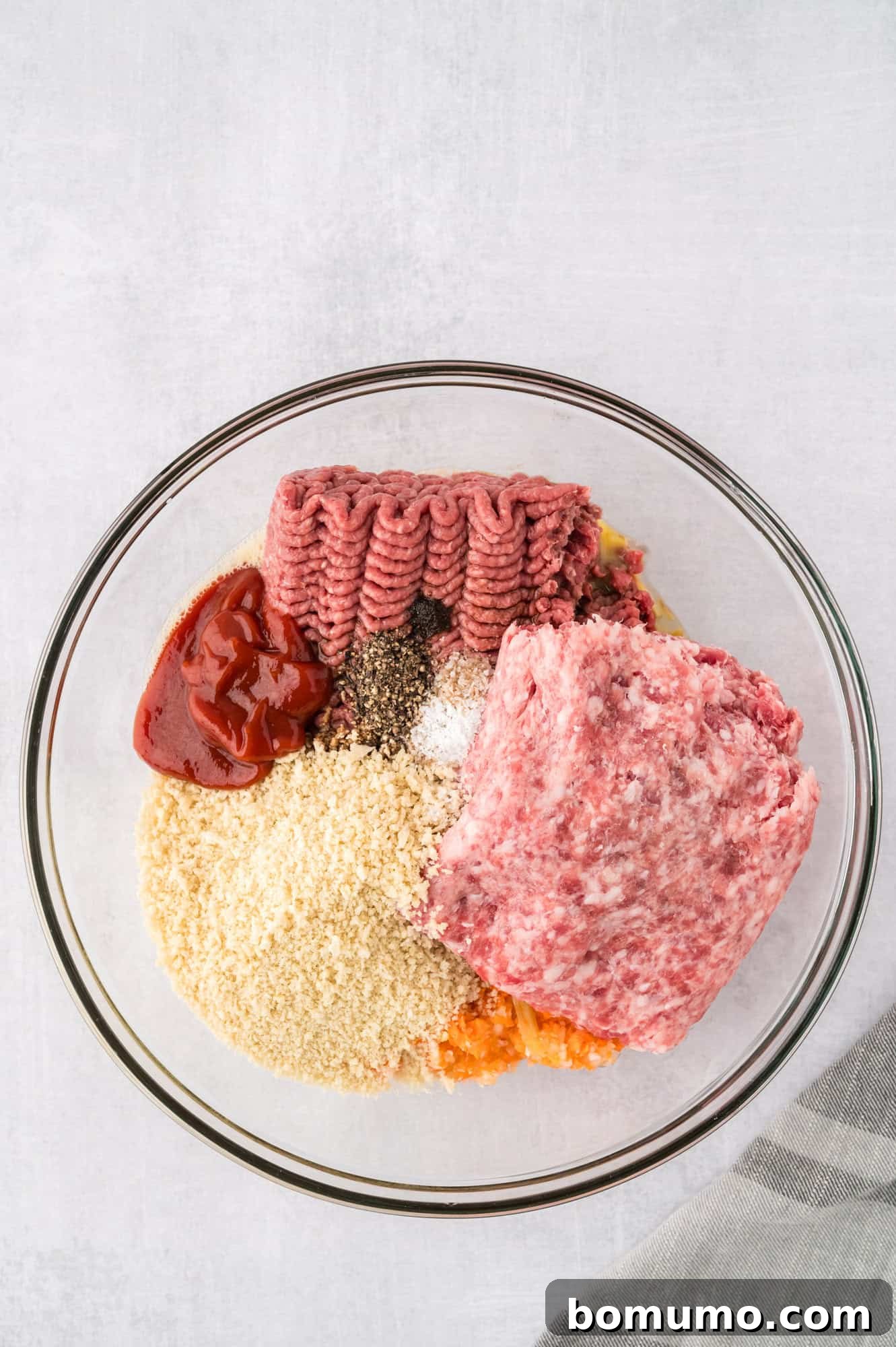 All crockpot meatloaf ingredients, including ground meat, breadcrumbs, milk, and seasonings, layered in a bowl before mixing.