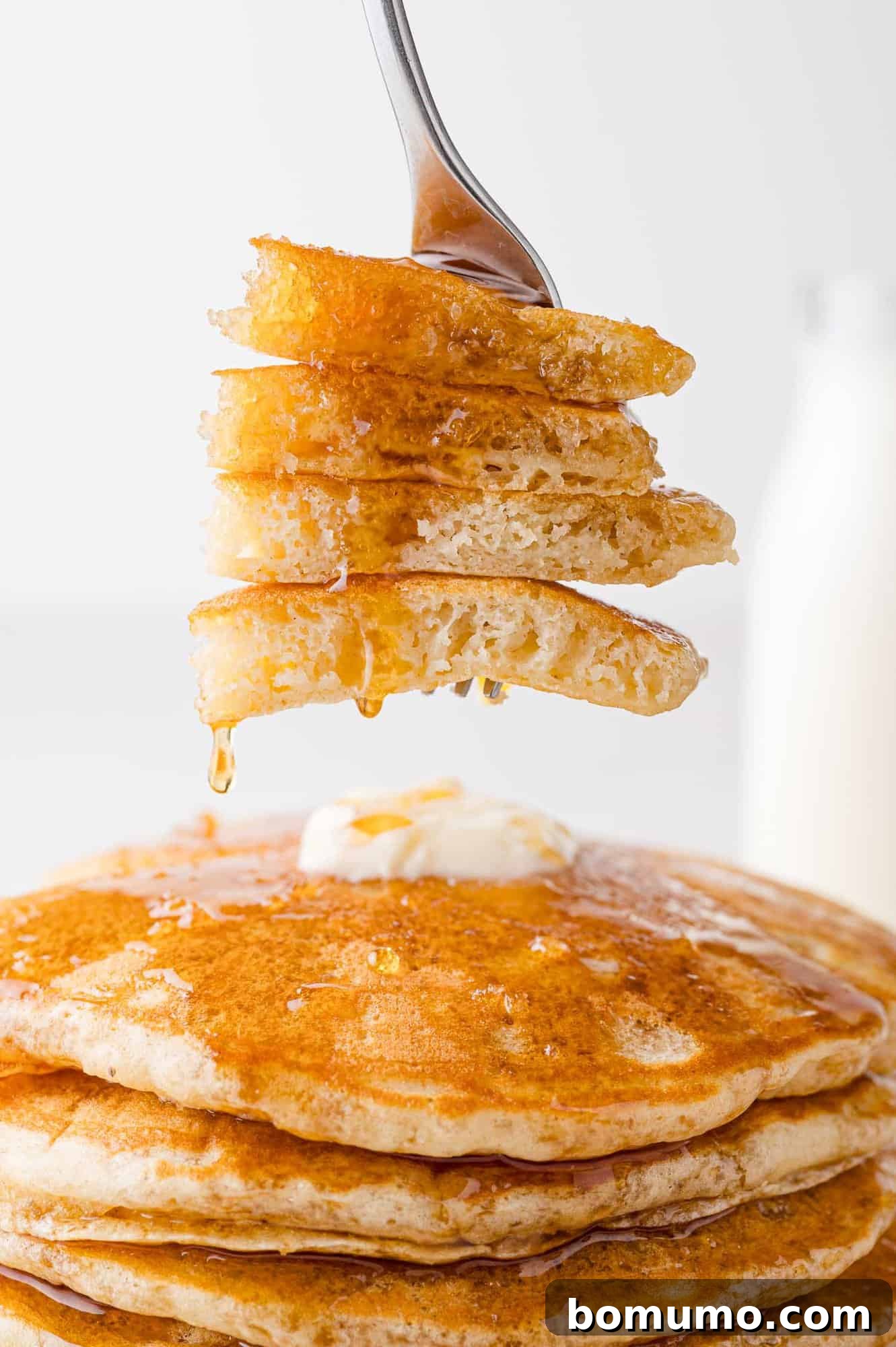 Buttermilk pancakes, cut and on a fork, showing texture. Syrup dripping off them.