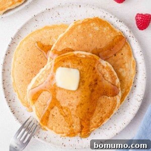 Overhead view of three buttermilk pancakes on a plate, with butter and syrup.