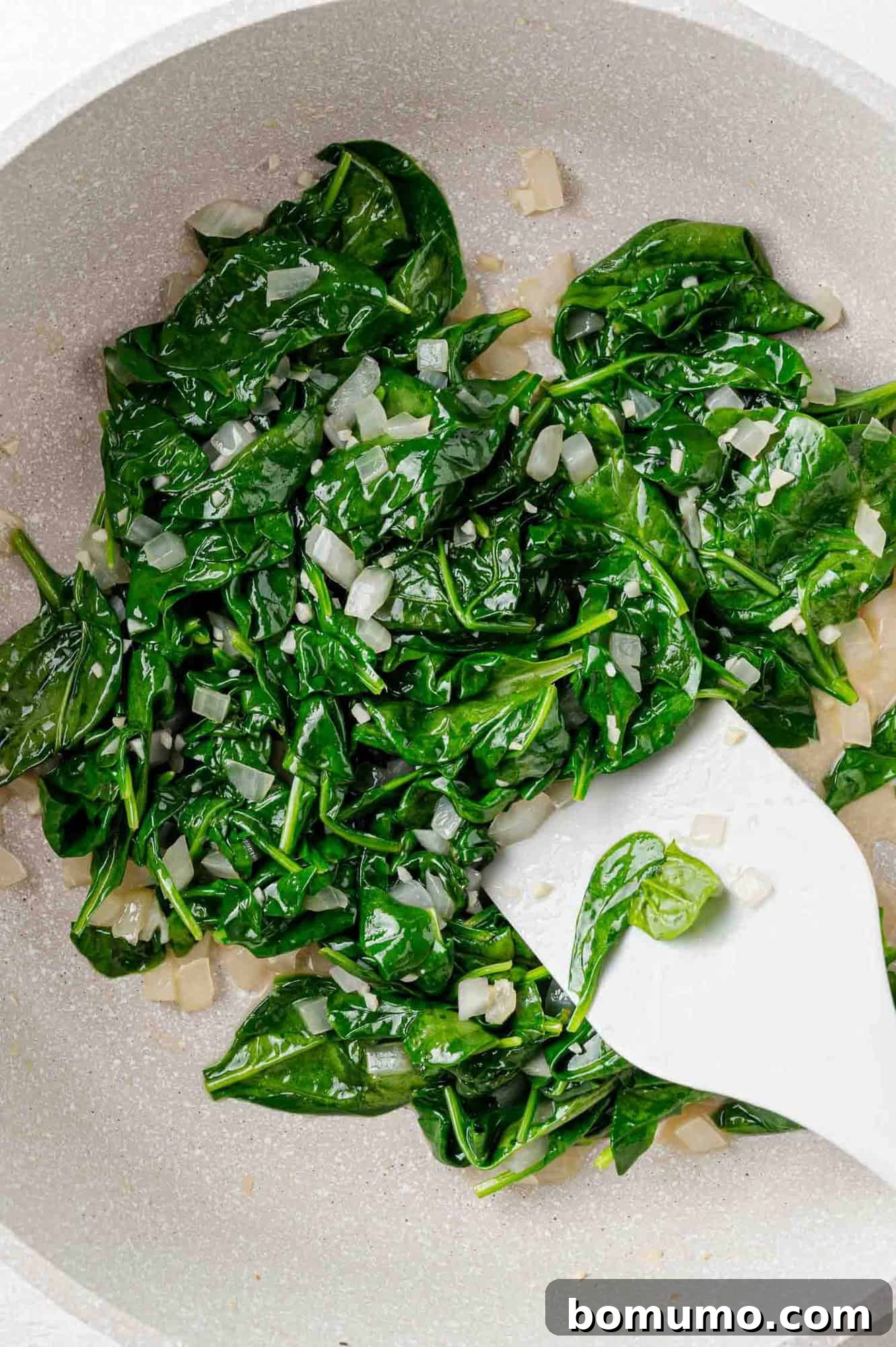 Silken Florentine Chicken 11 Wilted baby spinach being gently stirred into the aromatic mixture in the skillet with a spatula, creating a vibrant green base.