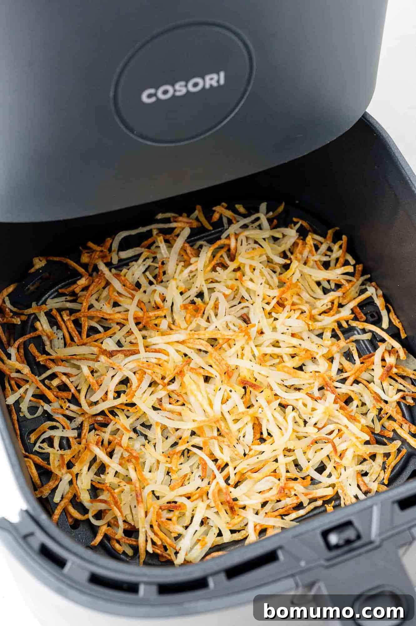 Crispy air fryer hash browns, still in the air fryer basket, perfectly golden brown.