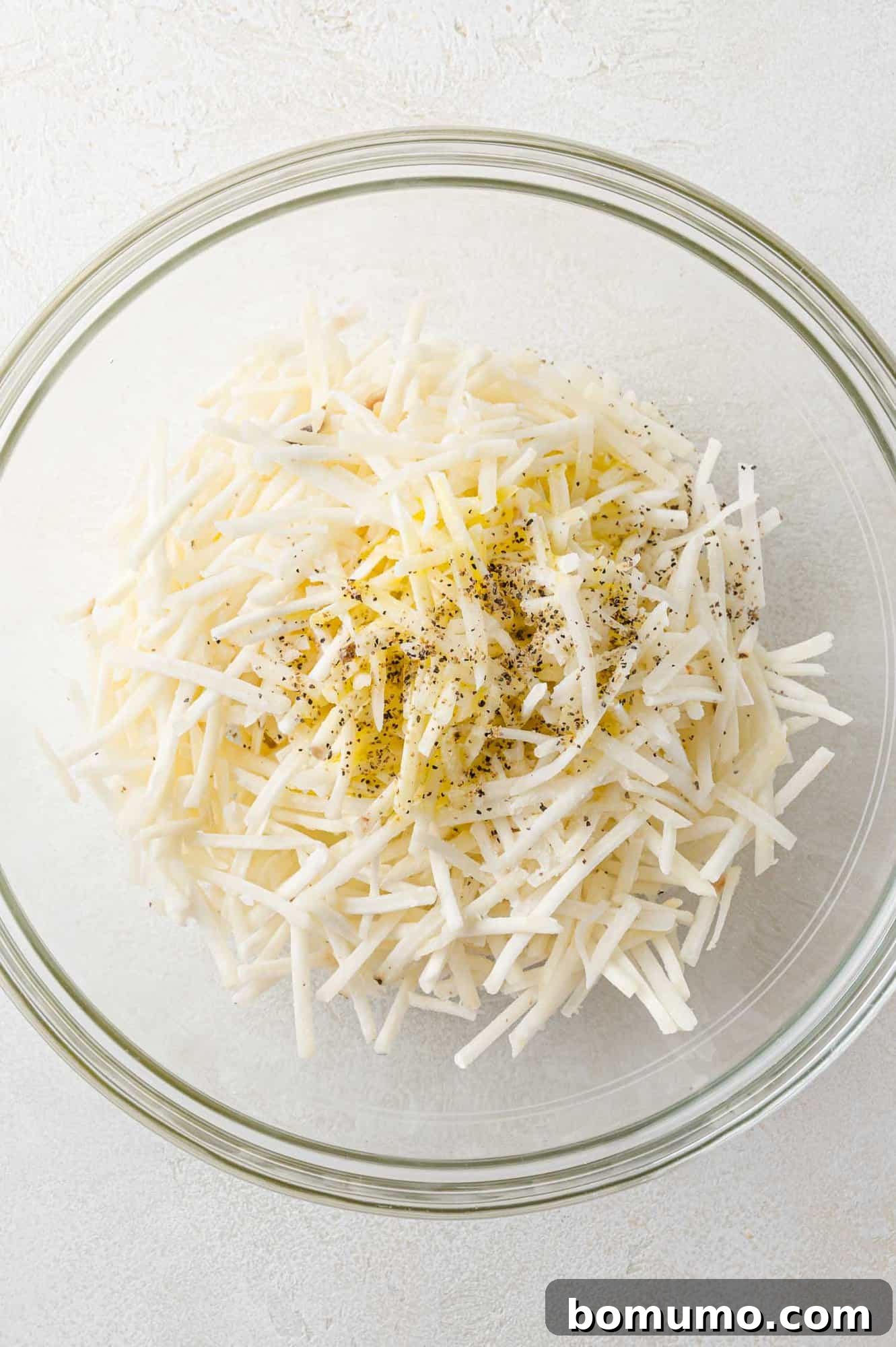 Seasonings added to a bowl of frozen hash browns, not yet mixed in.