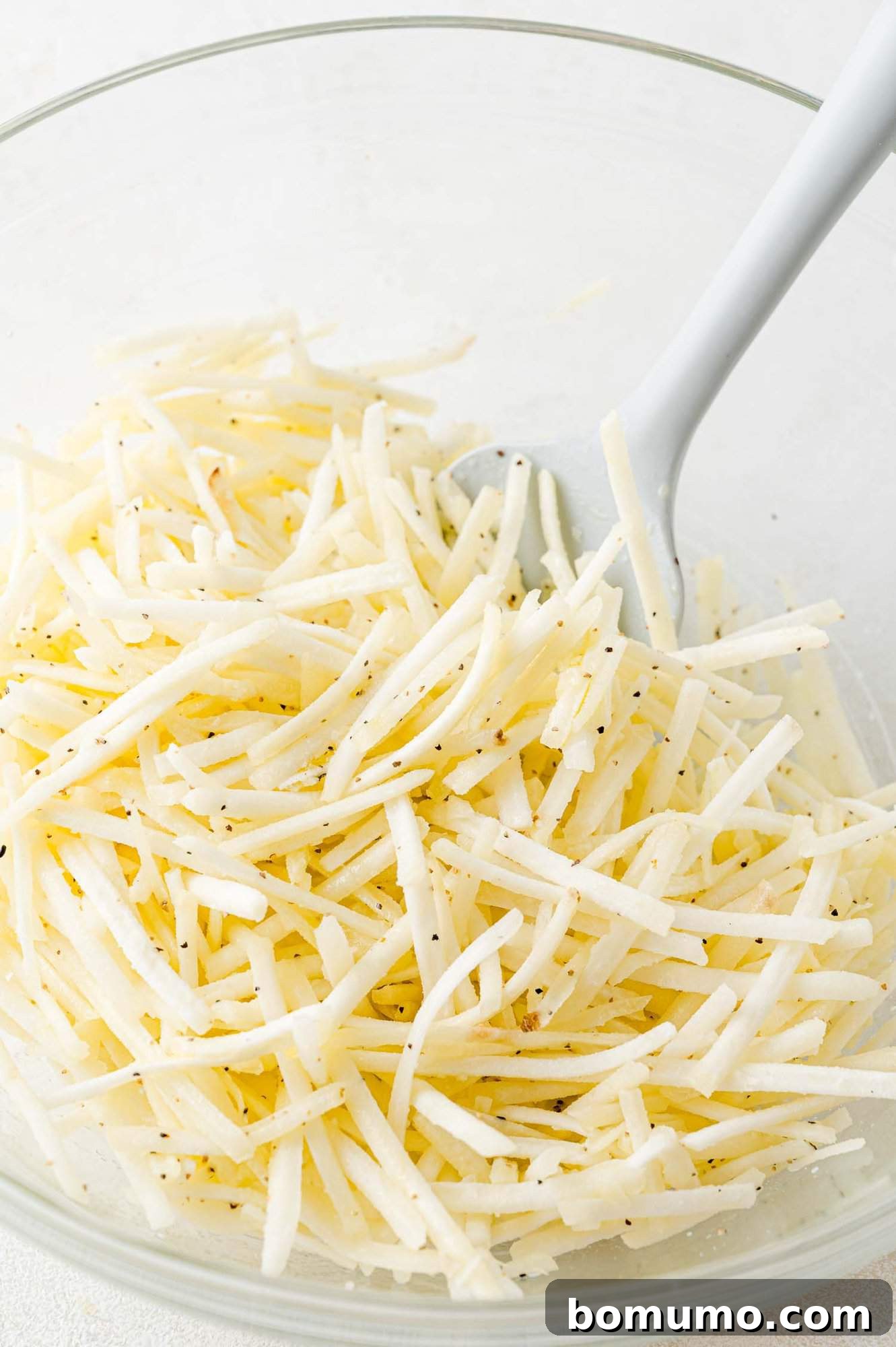 Hash browns mixed with seasonings and olive oil, in a clear glass bowl, ready for the air fryer.