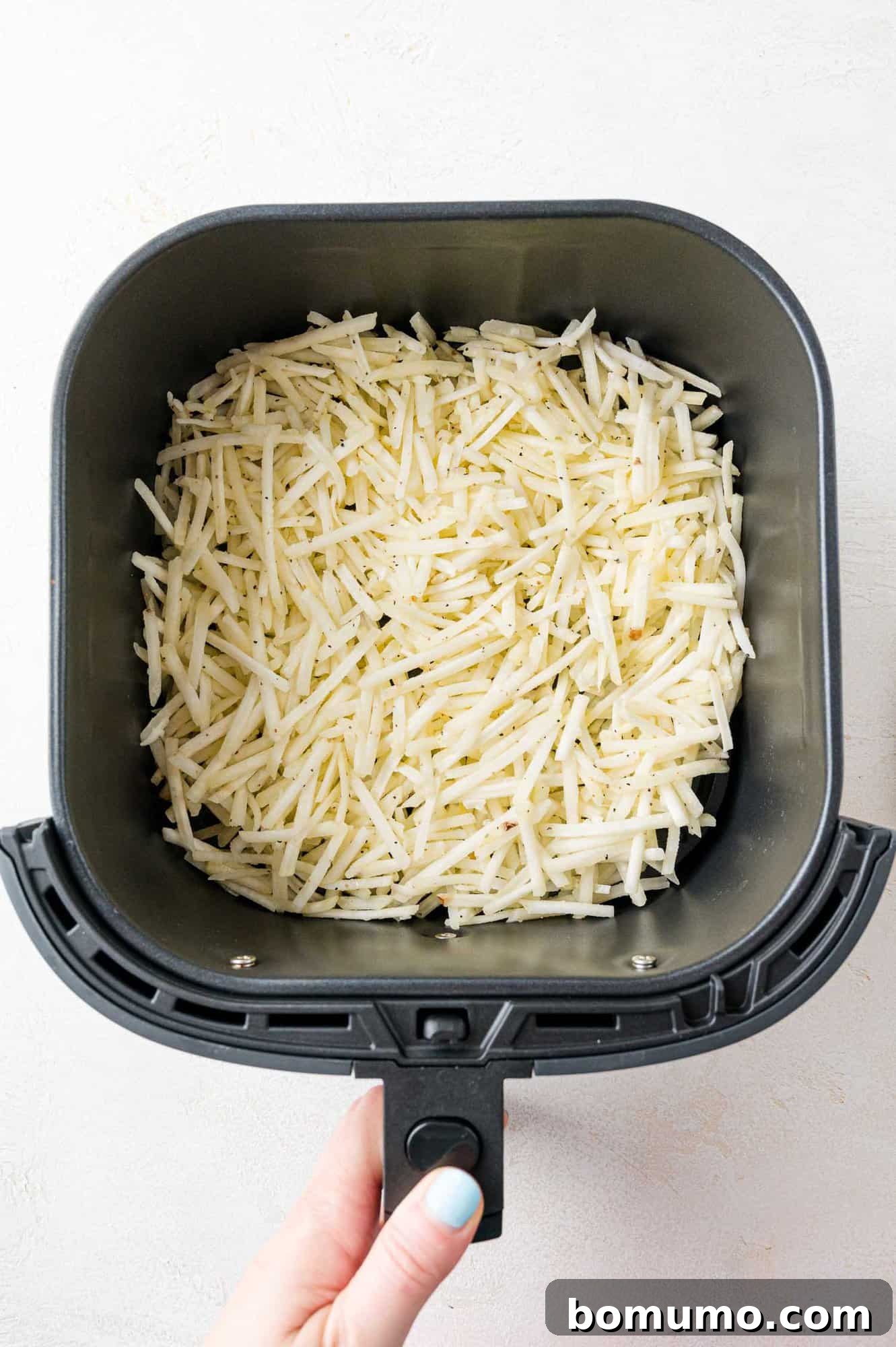 Hash browns spread evenly in an air fryer basket, before cooking.