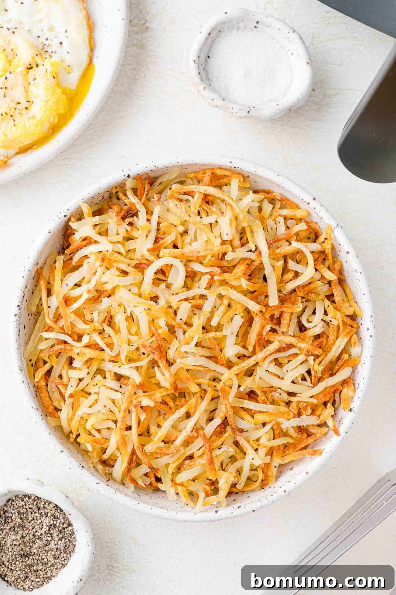 Air fryer hash browns served in a large white bowl, garnished with fresh parsley.