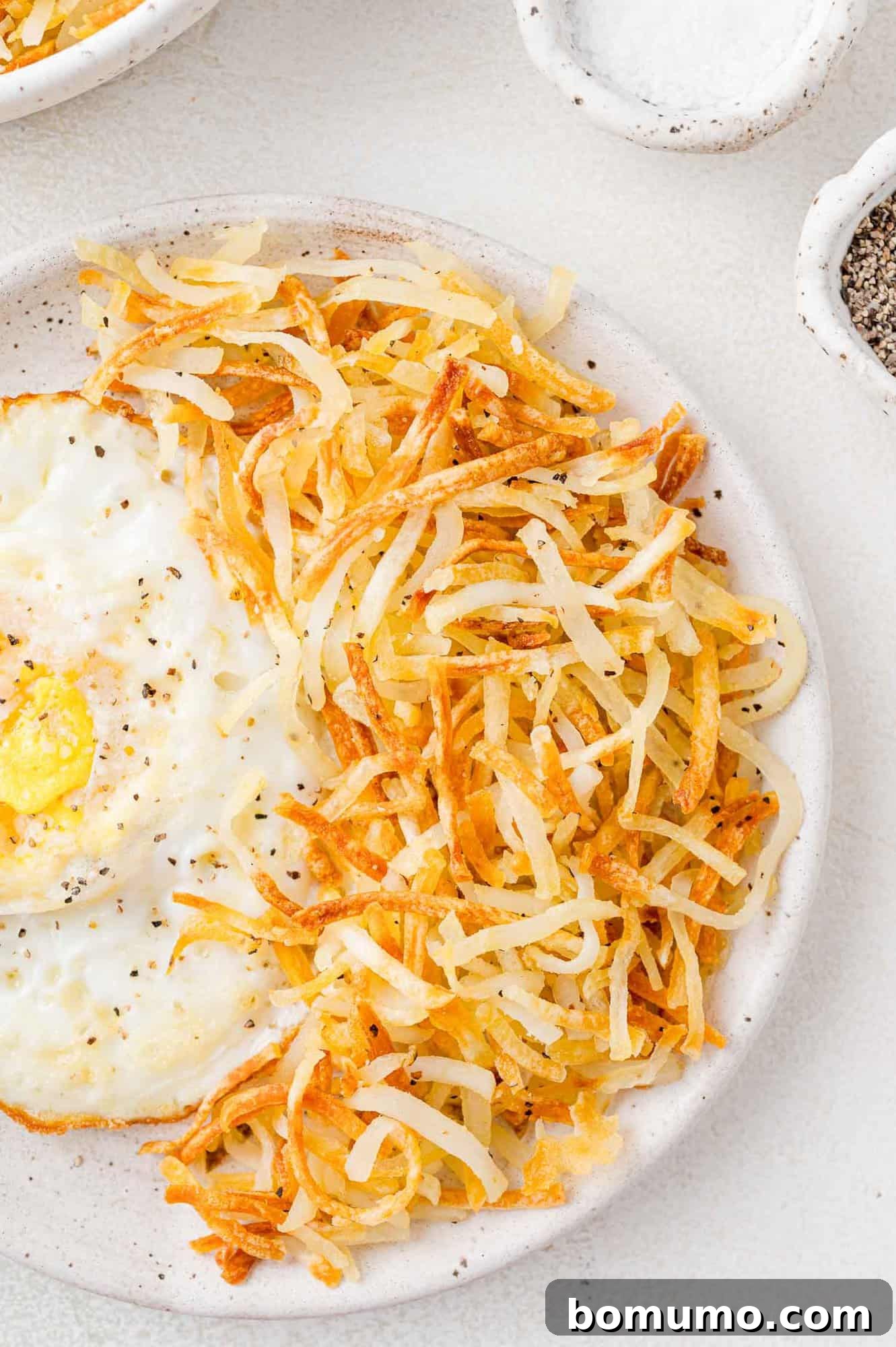 Crispy, golden brown hash browns on a white plate with a perfectly fried egg and fresh herbs.