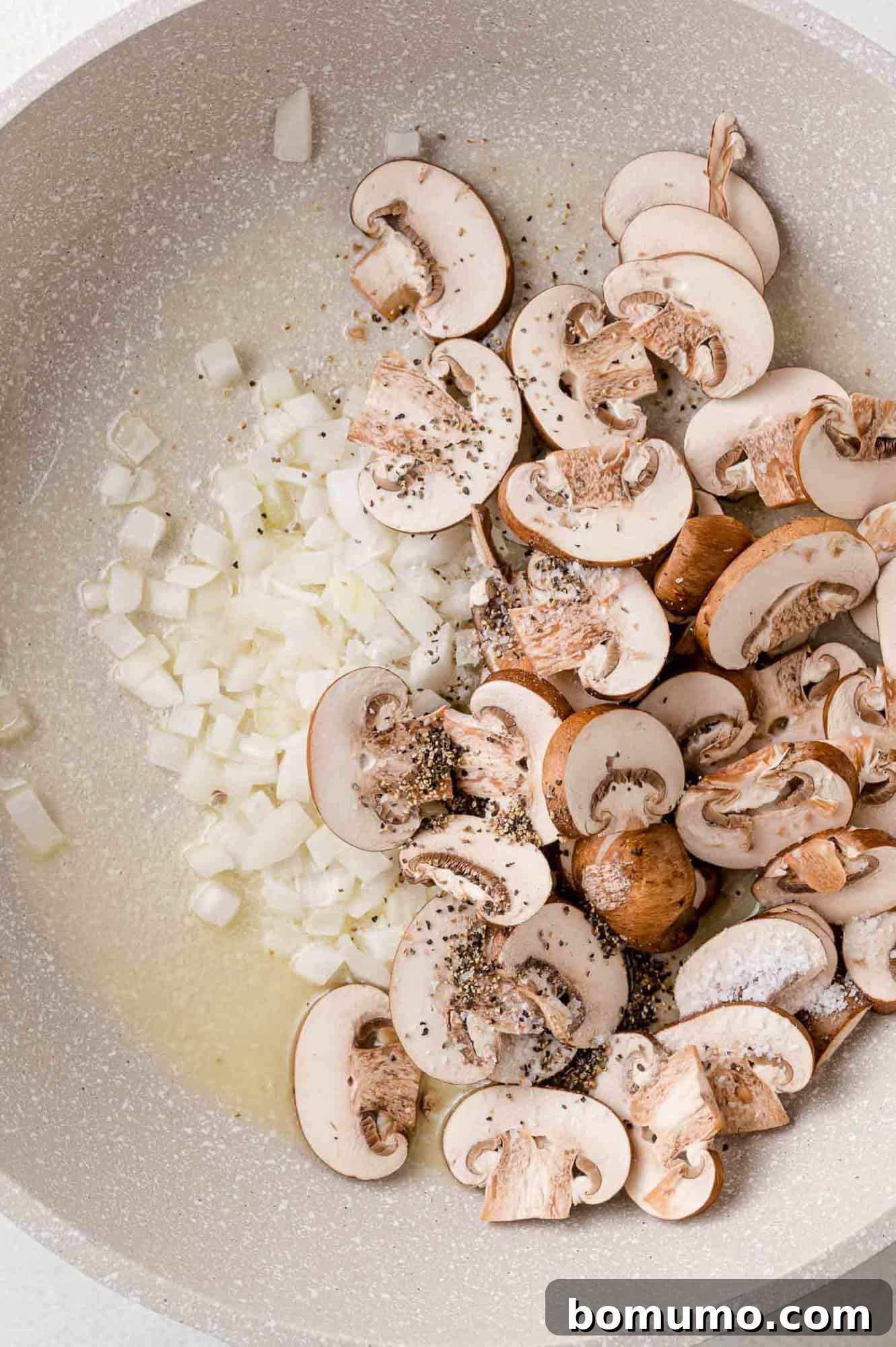 Uncooked onions, butter, and mushrooms resting in a pan before sautéing.