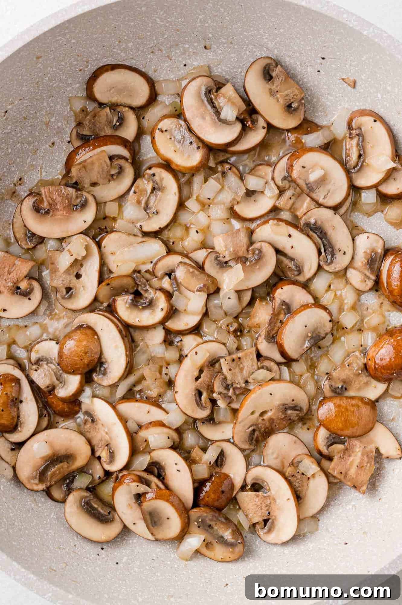 Sautéed mushrooms and onions, now softened and lightly golden in a skillet.