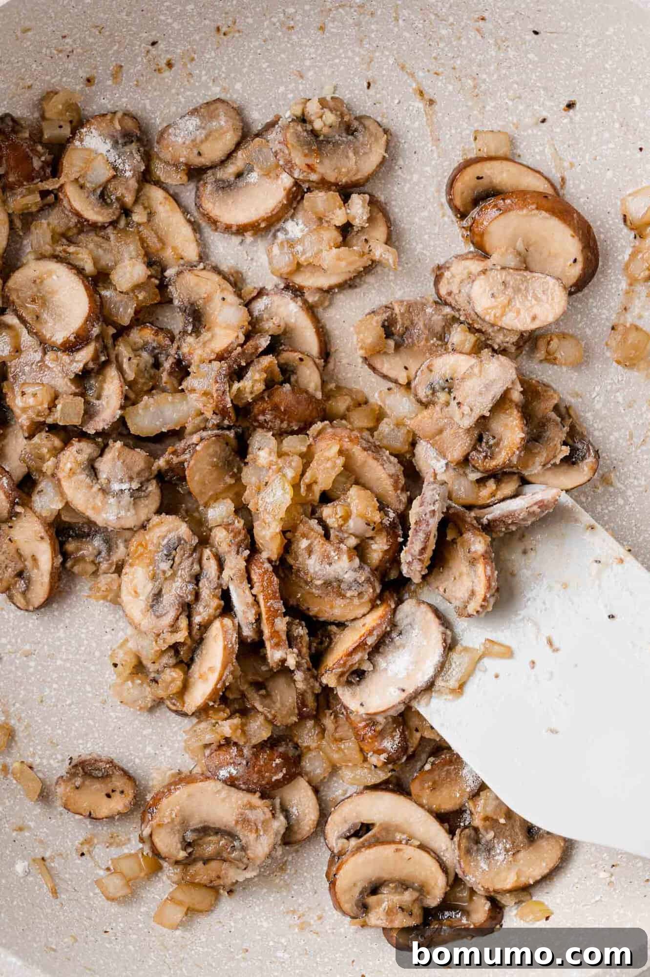 All-purpose flour dusted over the sautéed mushrooms and onions in the pan.