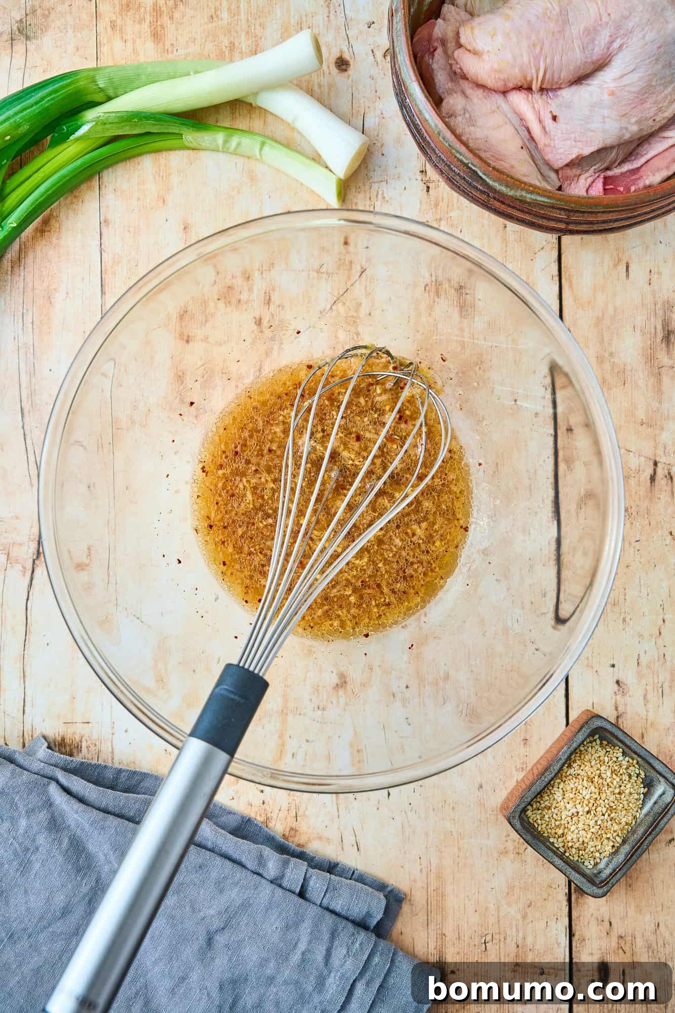 The vibrant ginger chicken marinade, a harmonious blend of liquids and spices, thoroughly mixed together in a clear glass bowl with a wire whisk.