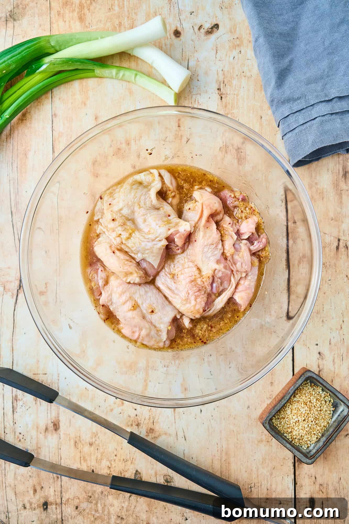 Raw chicken thighs carefully placed into the savory ginger marinade, ensuring each piece is well-coated and ready for flavor absorption.