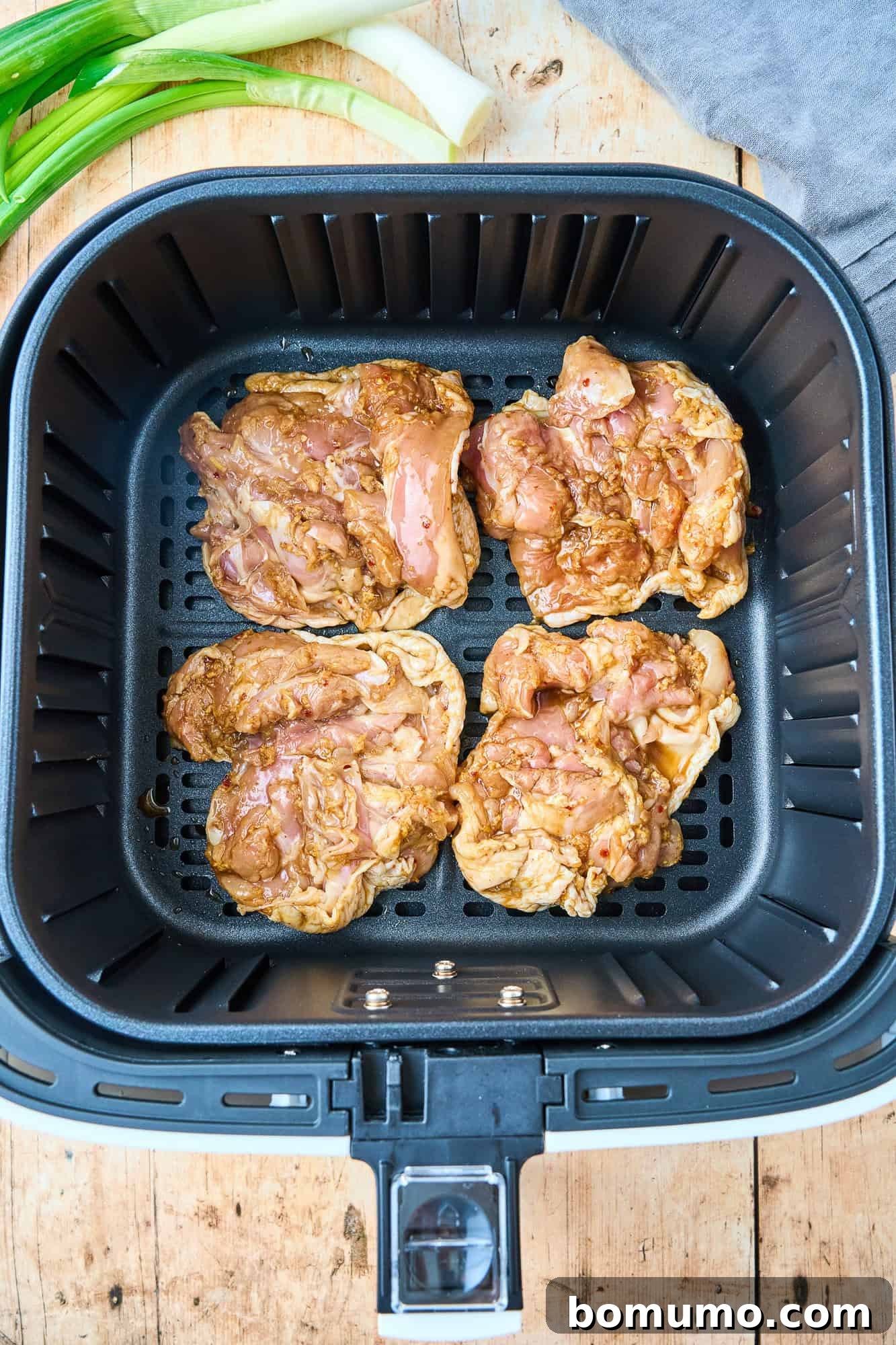 Raw chicken thighs, marinated and ready, neatly arranged skin-side down in the basket of an air fryer before cooking.