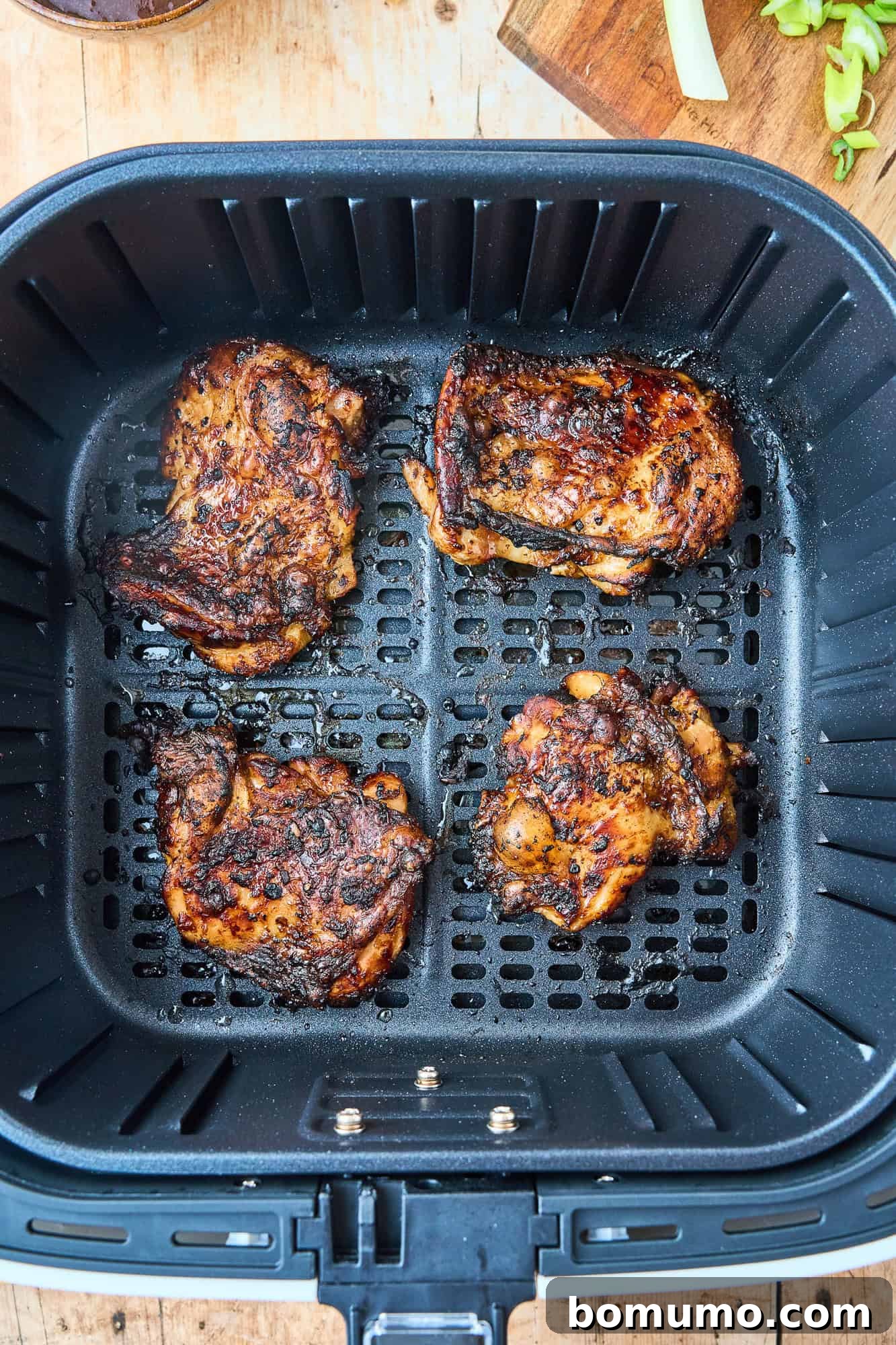 Perfectly cooked, golden-brown chicken thighs, with wonderfully crispy skin, resting in the air fryer basket, ready to be sauced and served.