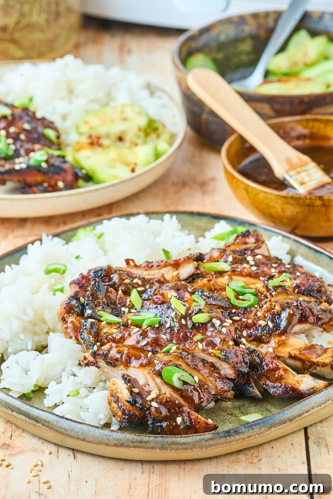 A beautifully plated dish featuring tender, sliced ginger chicken thigh on a bed of rice, with another full plate of the meal in the softly blurred background, suggesting a delightful dinner setting.