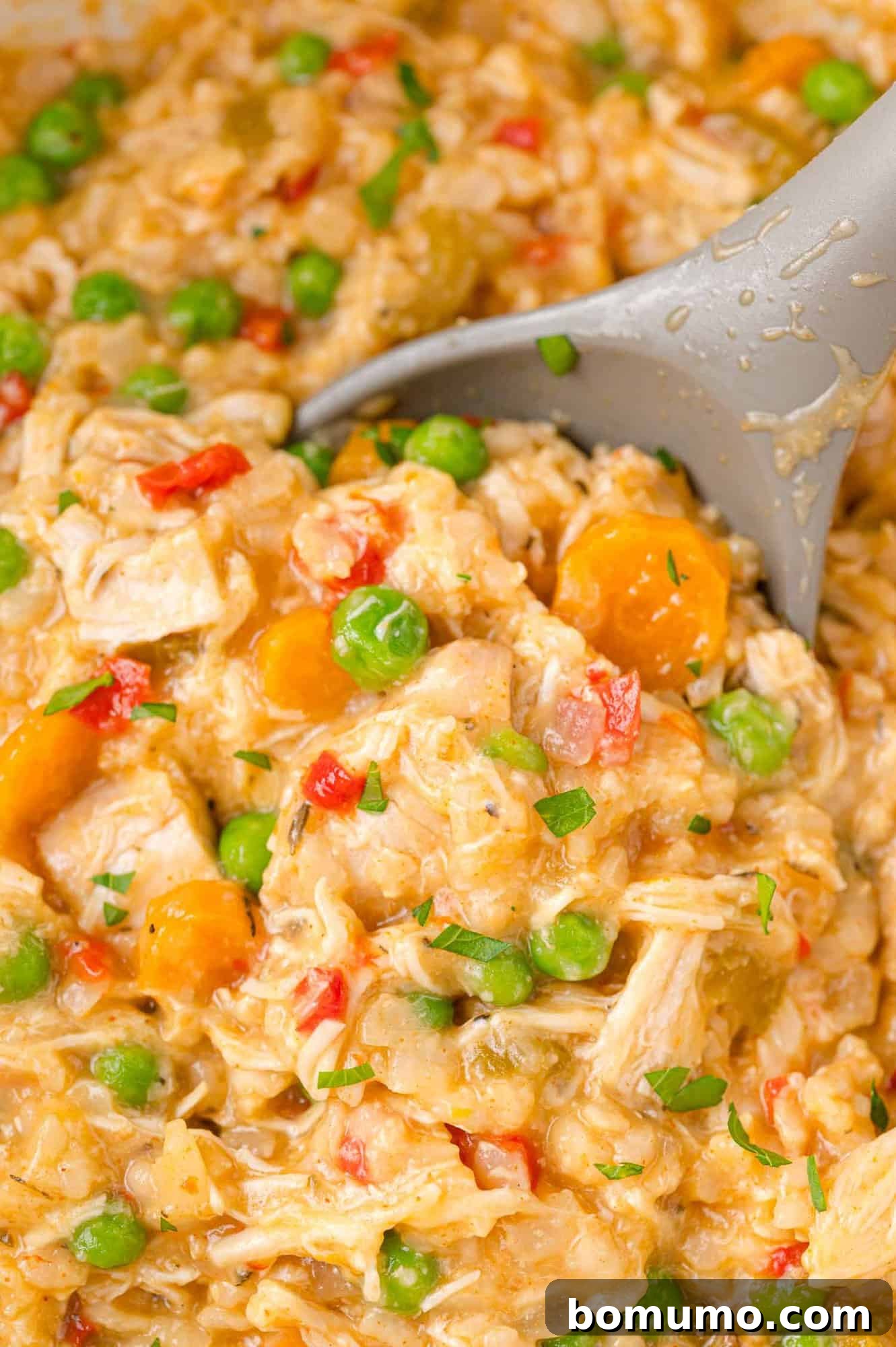 A serving spoon scoops up delicious Crockpot chicken and rice casserole, showcasing its creamy texture and tender ingredients.