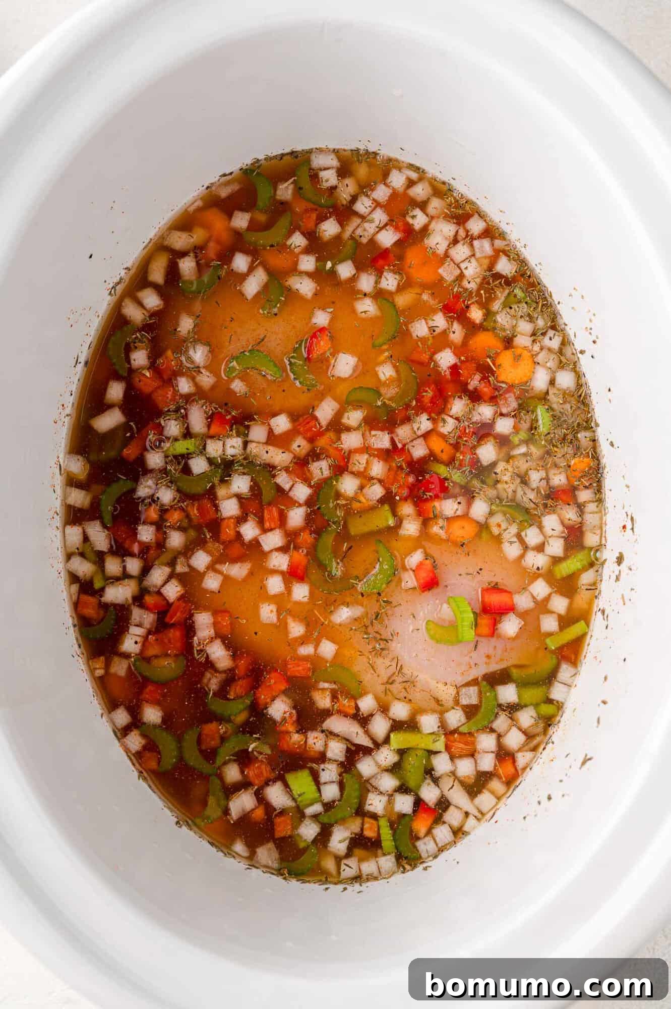 Broth has been added to the Crockpot chicken and rice ingredients, which are now ready for cooking.