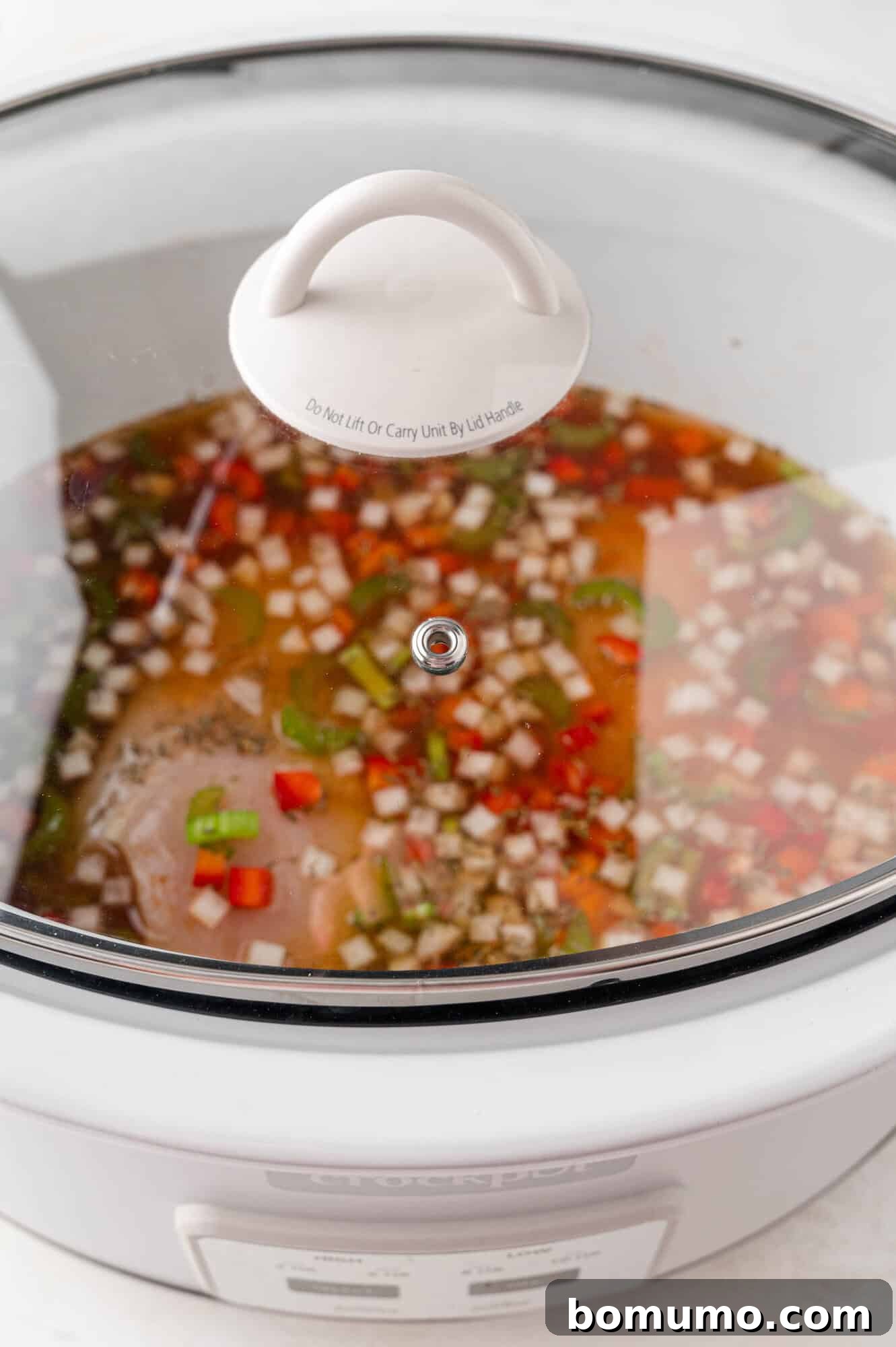 A white slow cooker with the lid on, simmering with the chicken and rice casserole inside.