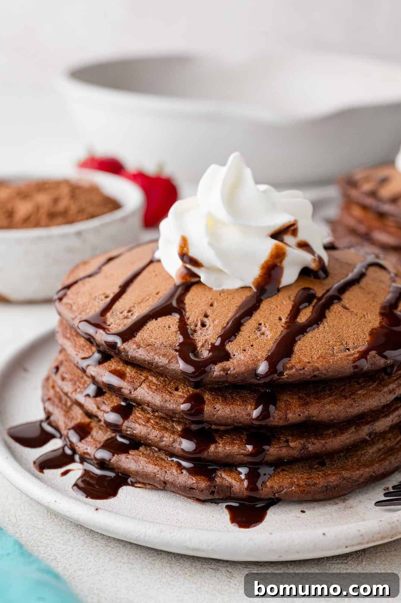 A stack of fluffy chocolate pancakes, drizzled generously with chocolate syrup and topped with a dollop of whipped cream, invitingly presented.