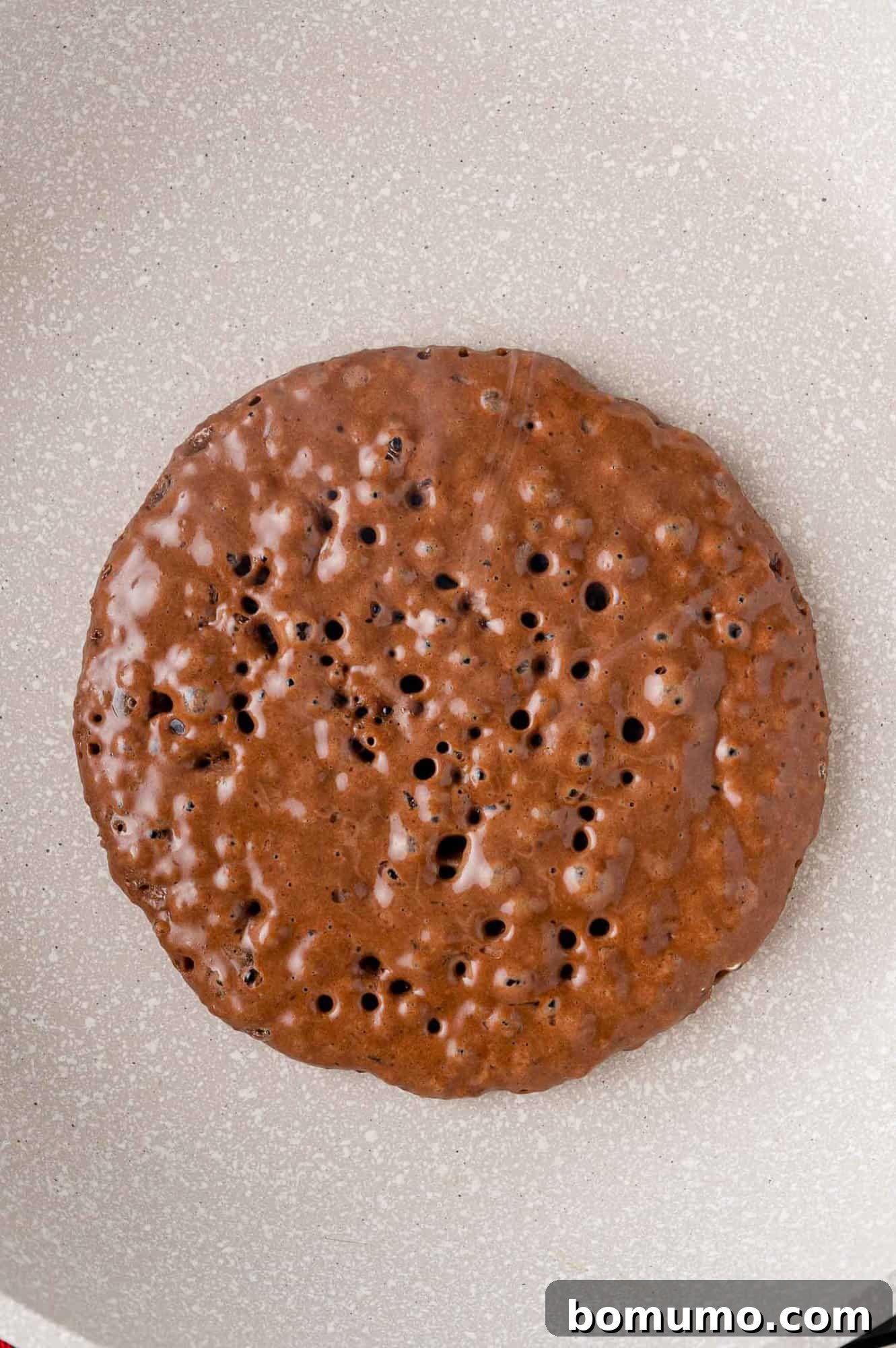 A perfectly cooked chocolate pancake on a griddle, golden brown and ready to be flipped.