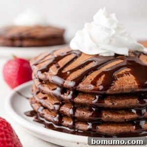 Stack of chocolate pancakes with chocolate syrup and whipped cream.