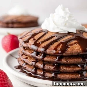 A stack of chocolate pancakes with chocolate syrup and whipped cream.