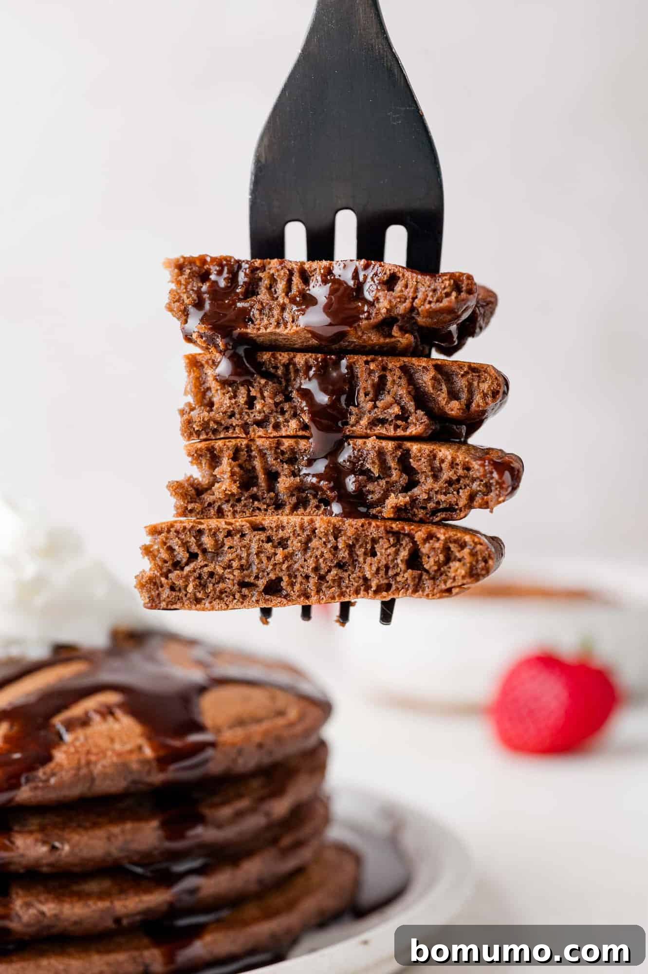 A chocolate pancake, expertly cut with a fork, revealing its soft, airy texture, highlighting the promise of a fluffy bite.