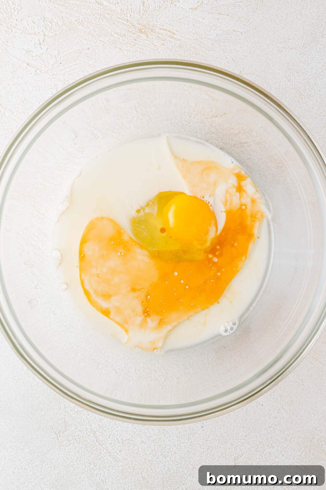 Wet ingredients for chocolate pancakes, including egg, milk, oil, and vanilla, in a bowl before mixing.