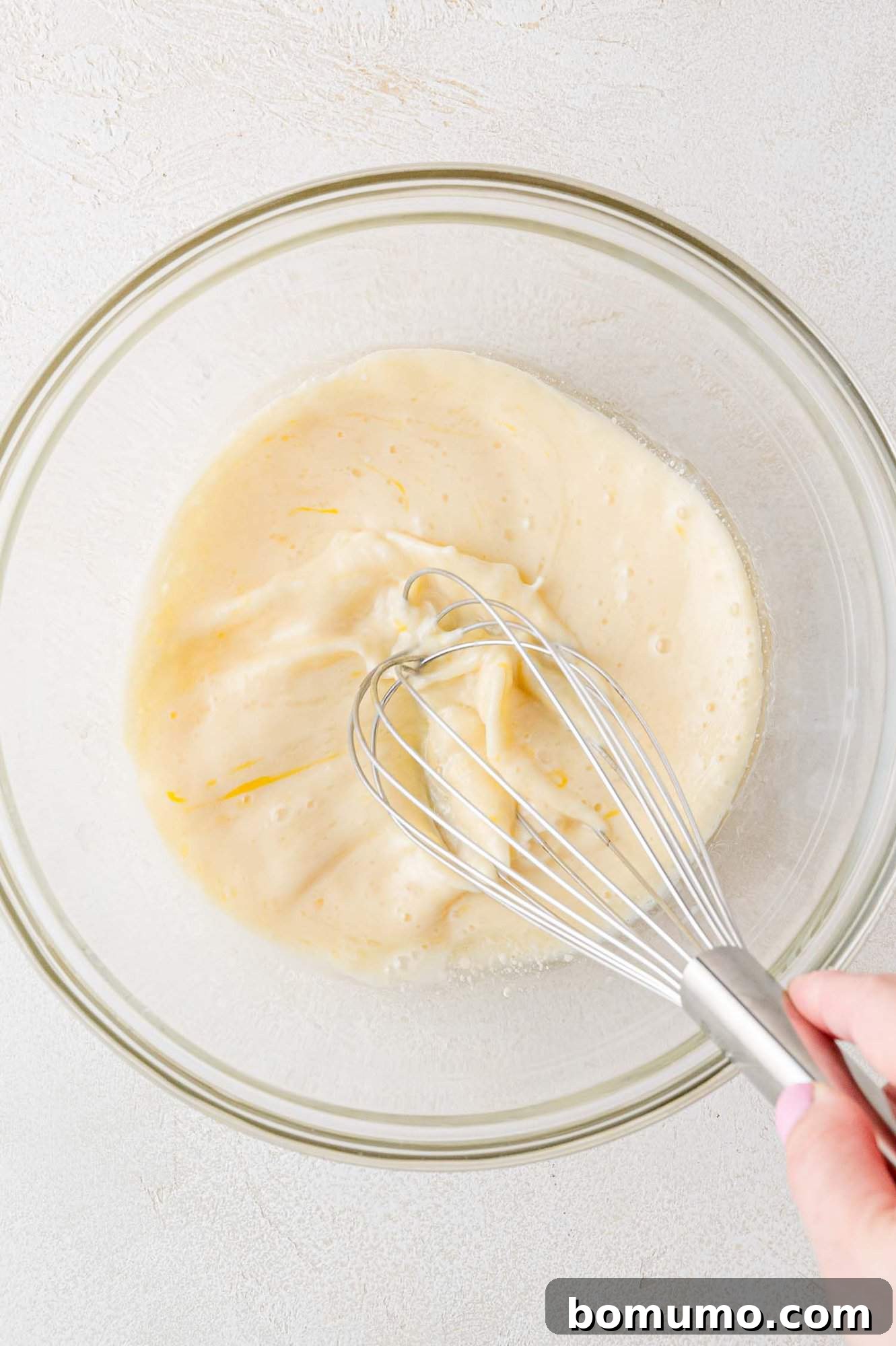 A hand whisking together the wet ingredients – egg, milk, oil, and vanilla – in a mixing bowl for pancake batter.