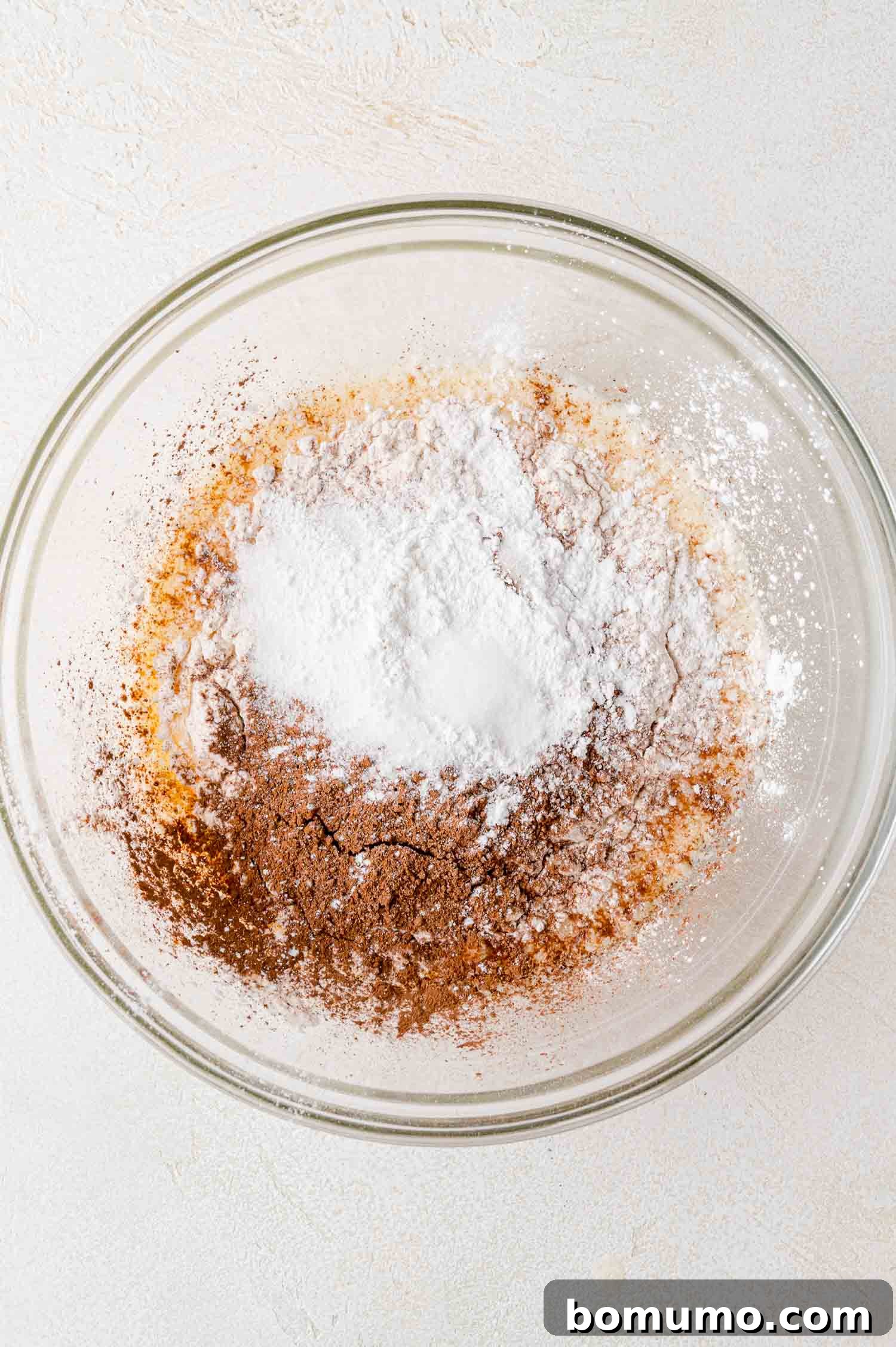 Dry ingredients like flour, cocoa powder, sugar, baking powder, and salt layered on top of wet ingredients in a bowl.