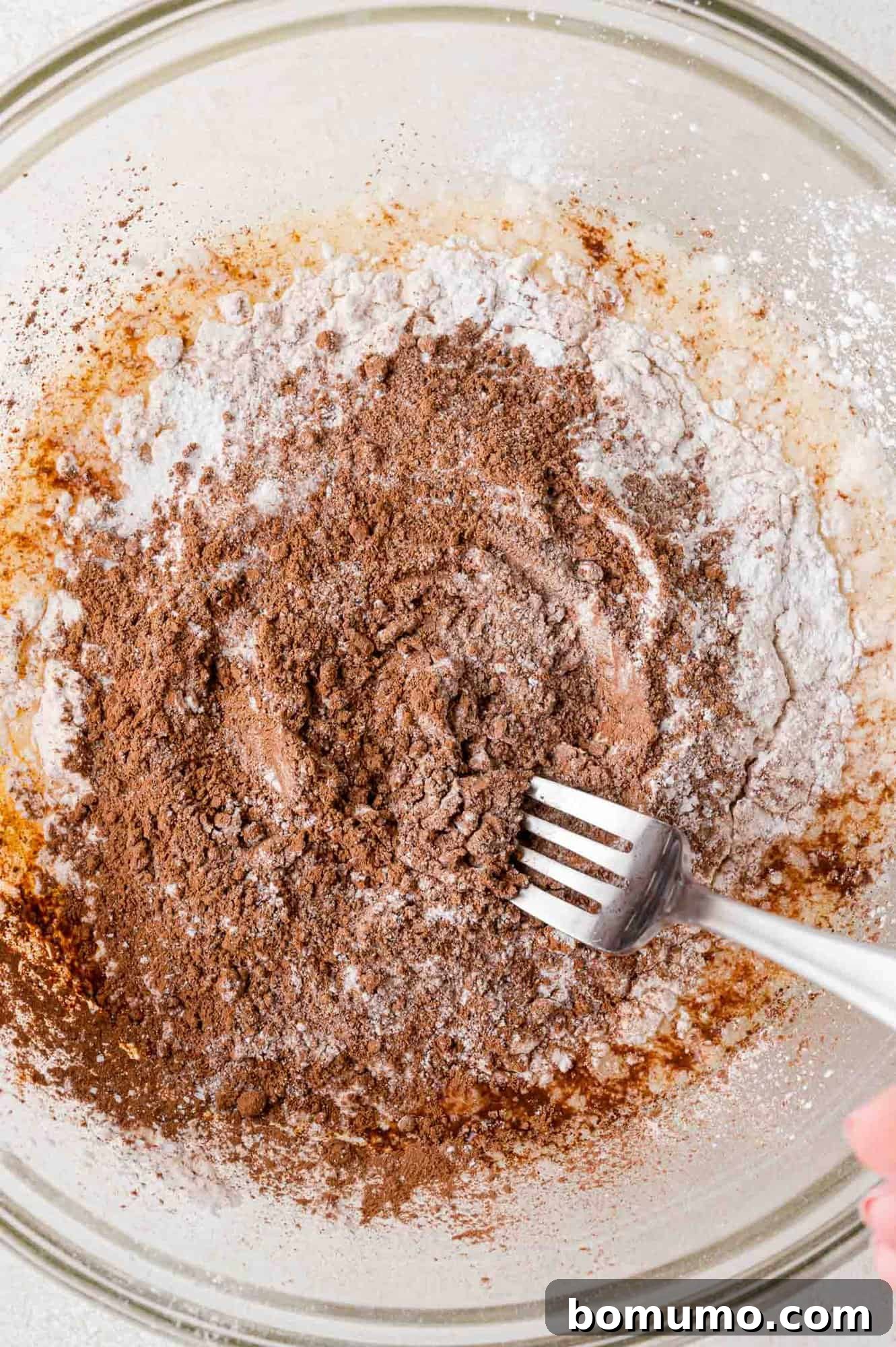 A fork lightly mixing the dry ingredients together on top of the wet ingredients in a bowl.