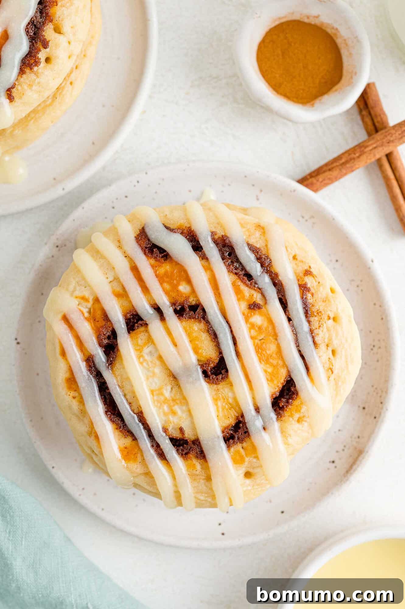 Cinnamon Swirl Flapjacks 2 Overhead view of cinnamon roll pancakes on a small plate, cinnamon next to it.