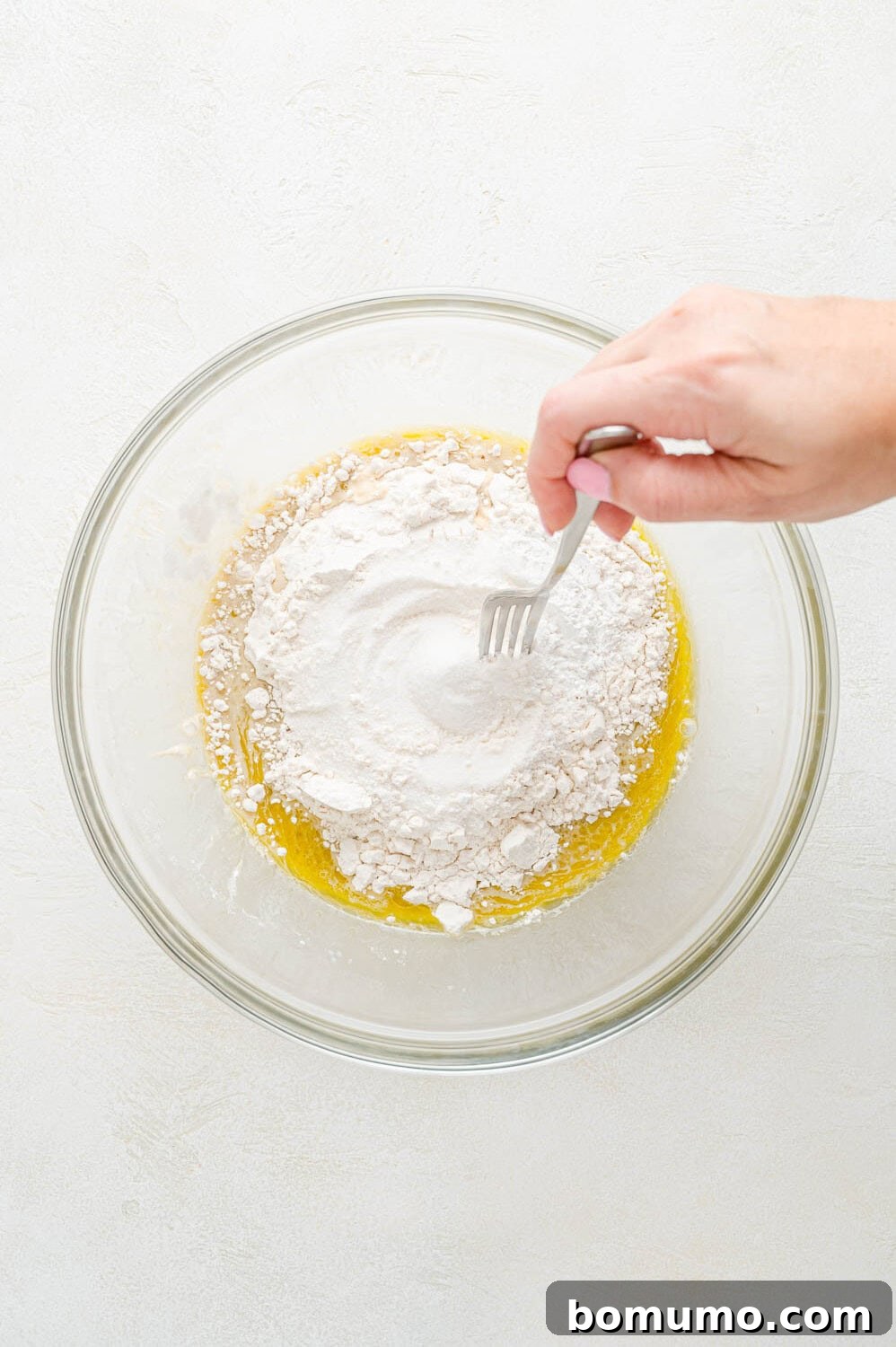 Cinnamon Swirl Flapjacks 8 Dry ingredients being added to wet ingredients in a clear glass mixing bowl.
