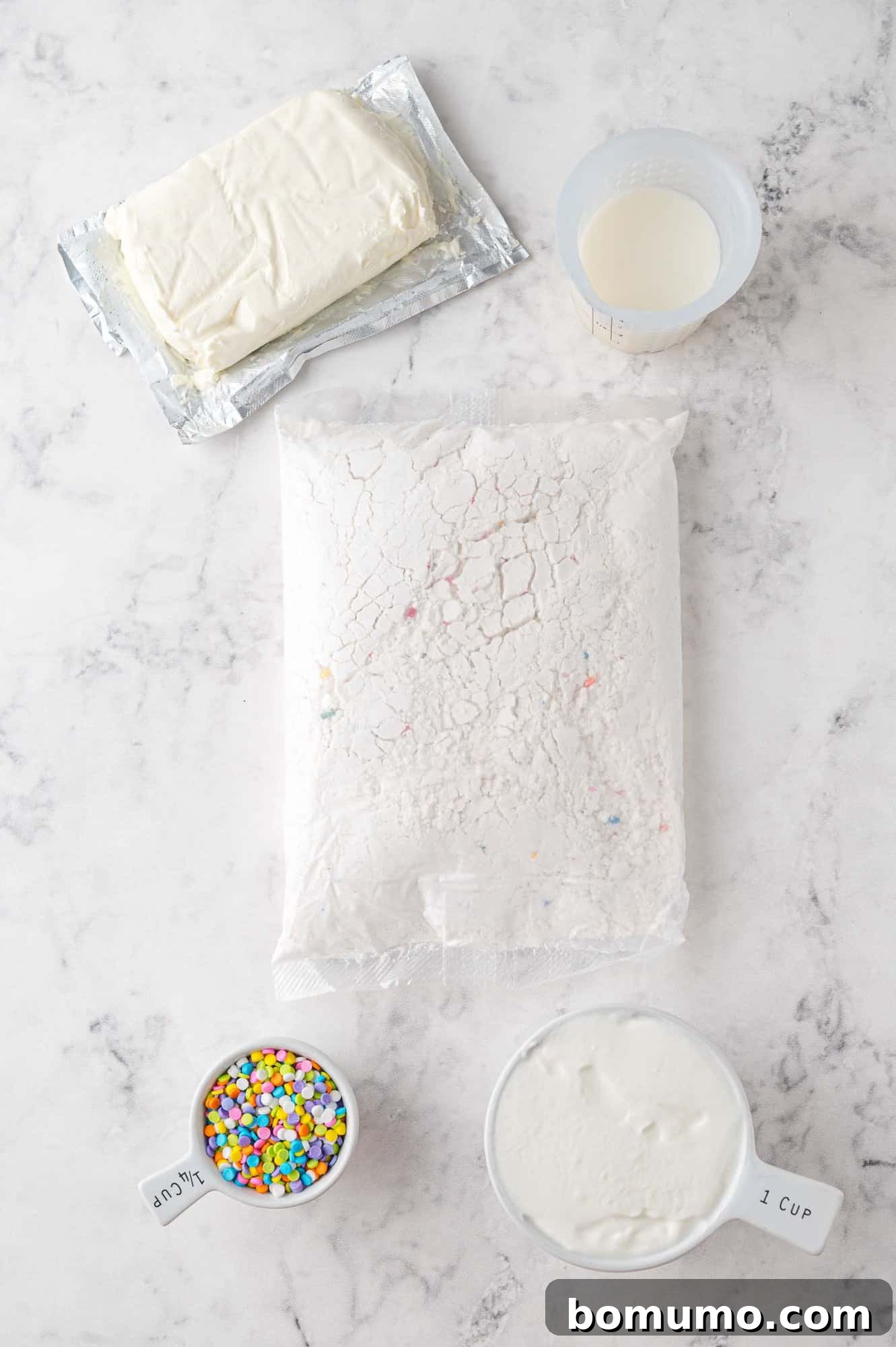 A collection of essential ingredients for Funfetti Dip arranged on a pristine marble surface: a box of Funfetti cake mix, a block of softened cream cheese, a cup of fresh milk, a container of plain Greek yogurt, and a small bowl overflowing with colorful sprinkles. Each item is perfectly positioned to begin the baking process.