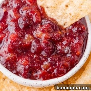 Cranberry salsa in a white bowl, with a chip dipping into it.