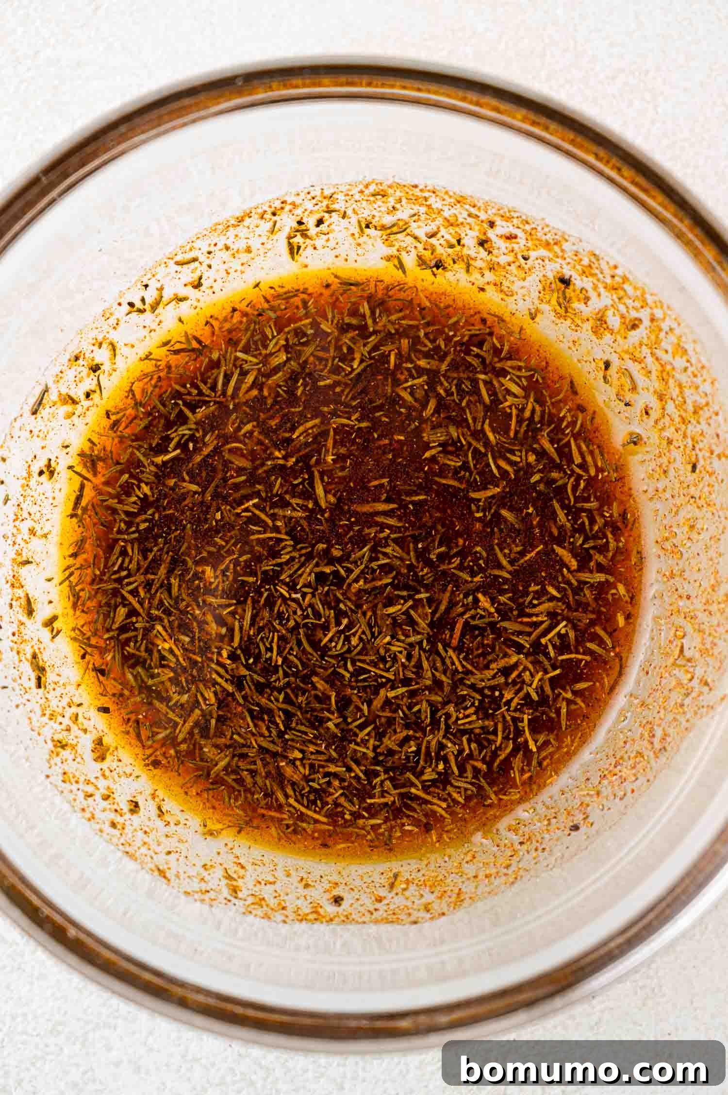 A glass bowl containing a brown liquid mixture with herbs and spices.