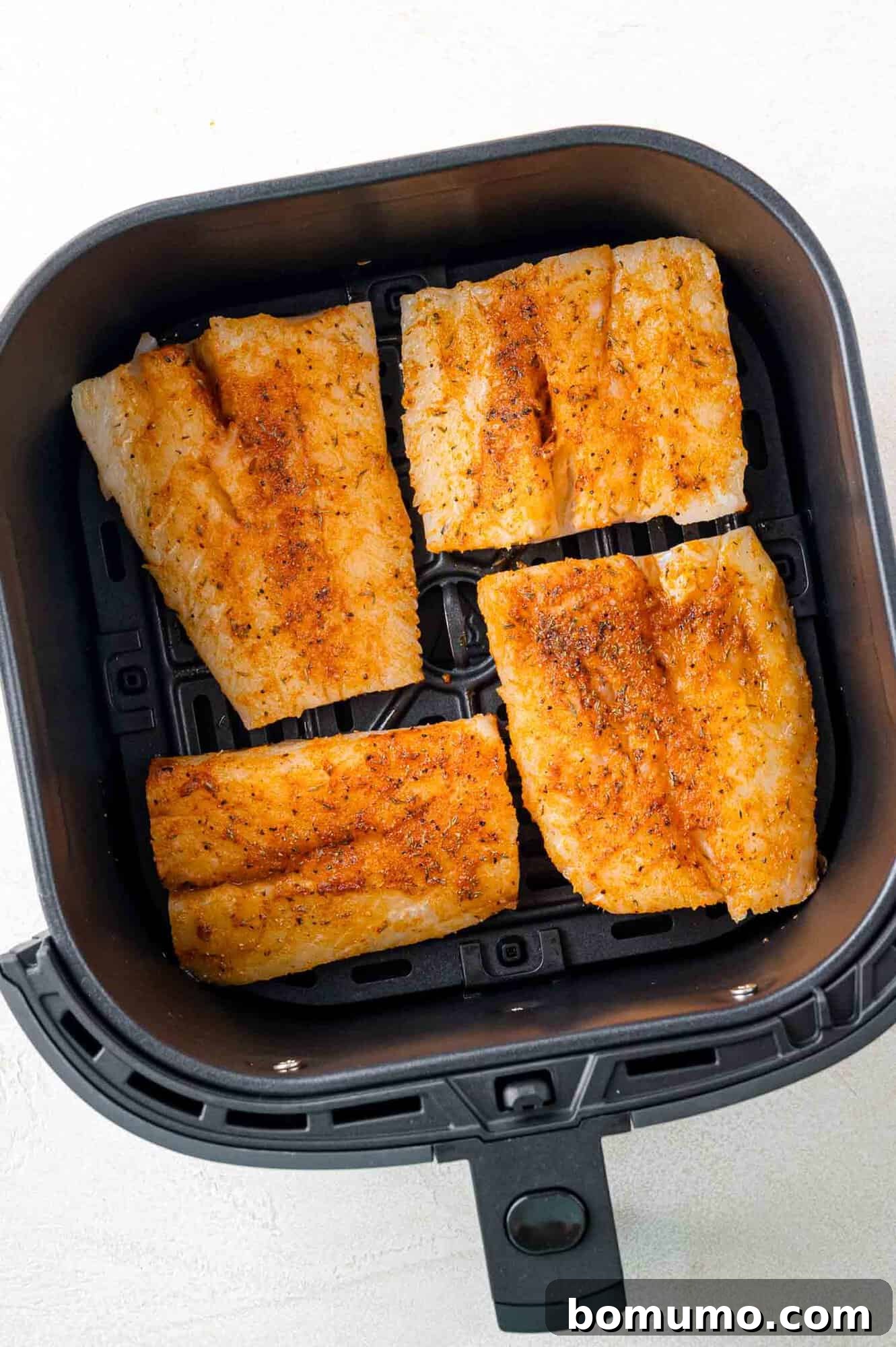 Four pieces of seasoned fish fillets are placed in an air fryer basket, ready for cooking.